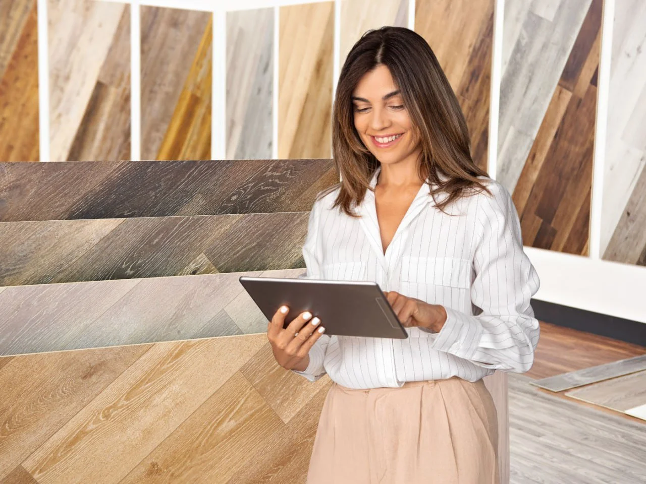 Woman shopping for wood flooring options using a tablet in a flooring store.