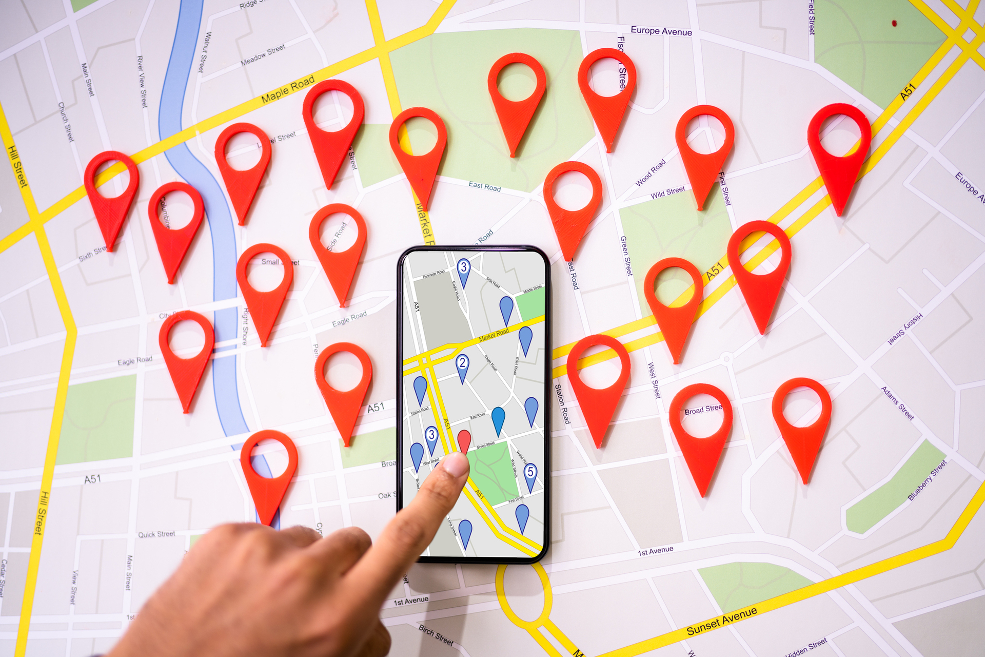 A person using a smartphone to navigate in a map with red location markers placed on various points of interest on a city street map.