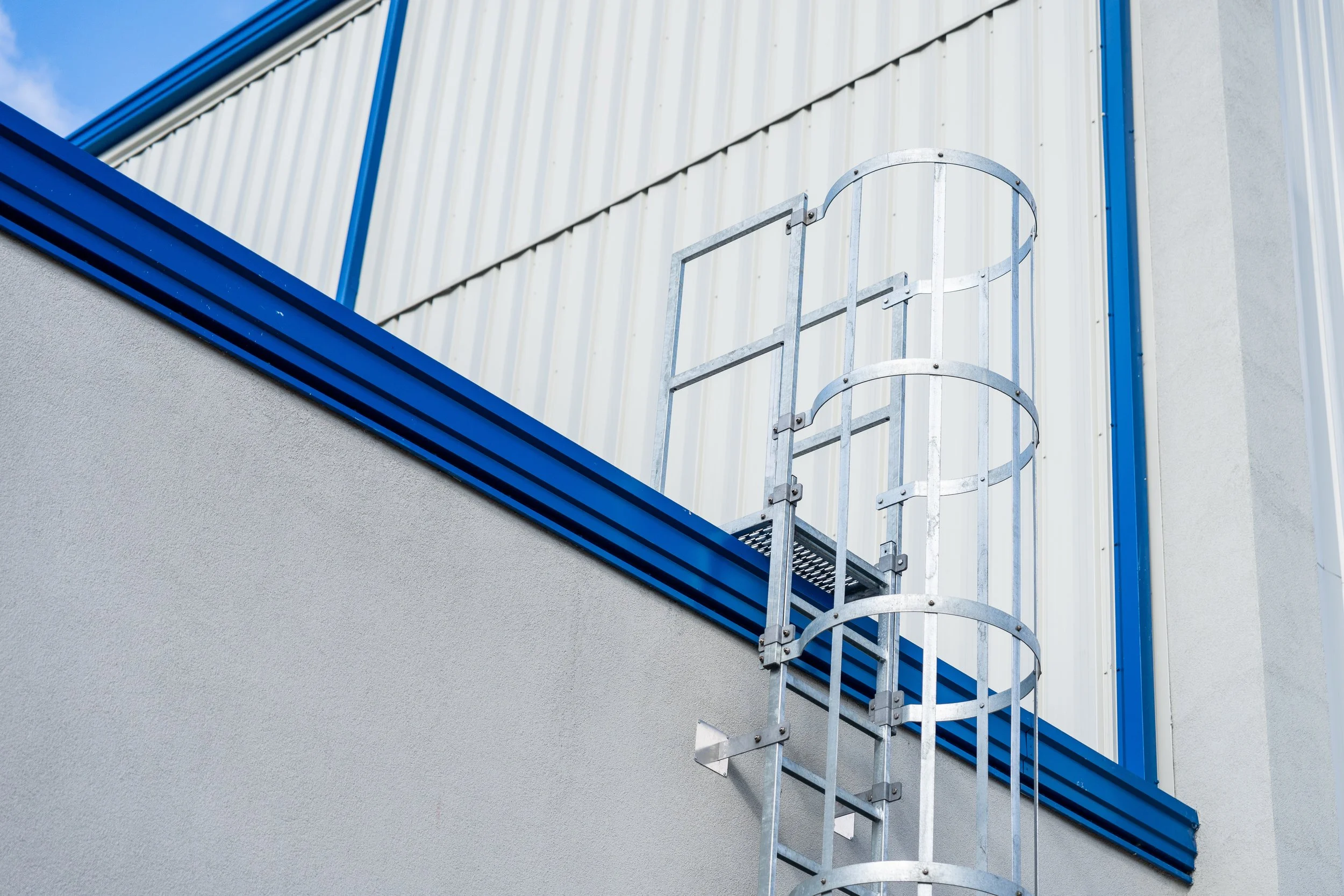 Metal fire escape ladder attached to the side of a building with white and blue exterior walls.