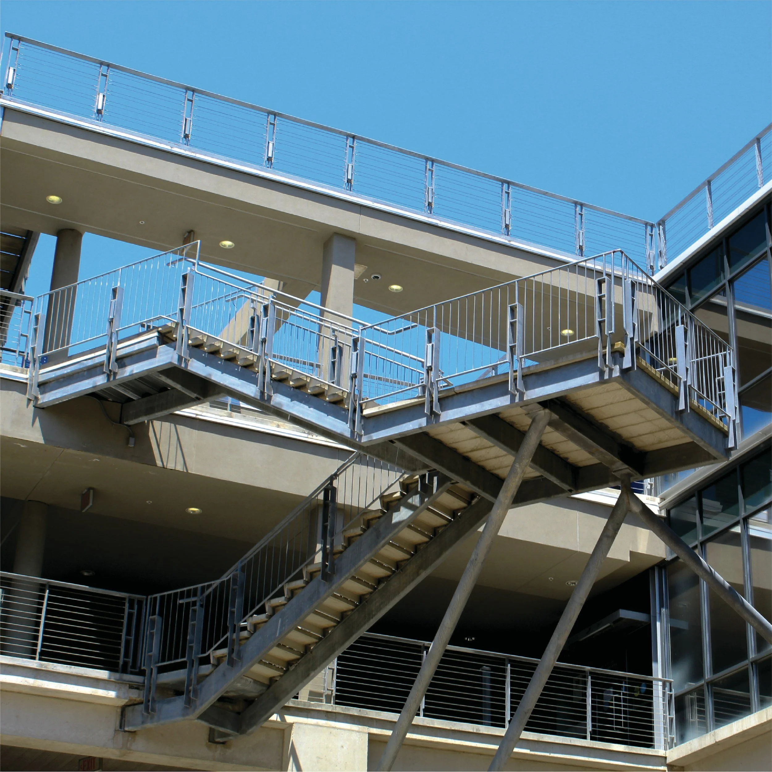 Modern building exterior with steel fire escape staircase against a clear blue sky.