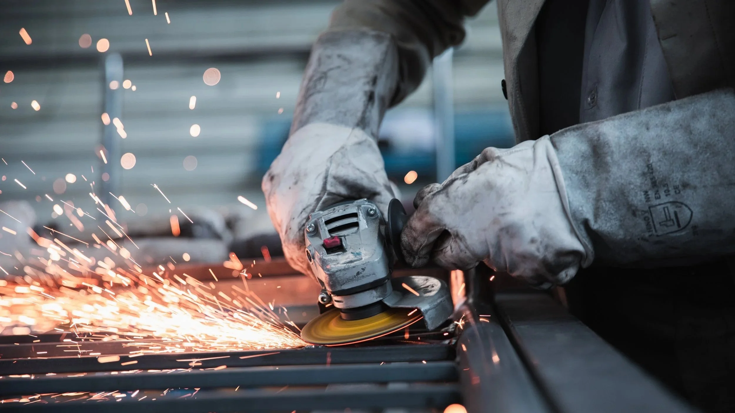 A worker cutting metal with an angle grinder, sparks flying as the tool makes contact with the surface.