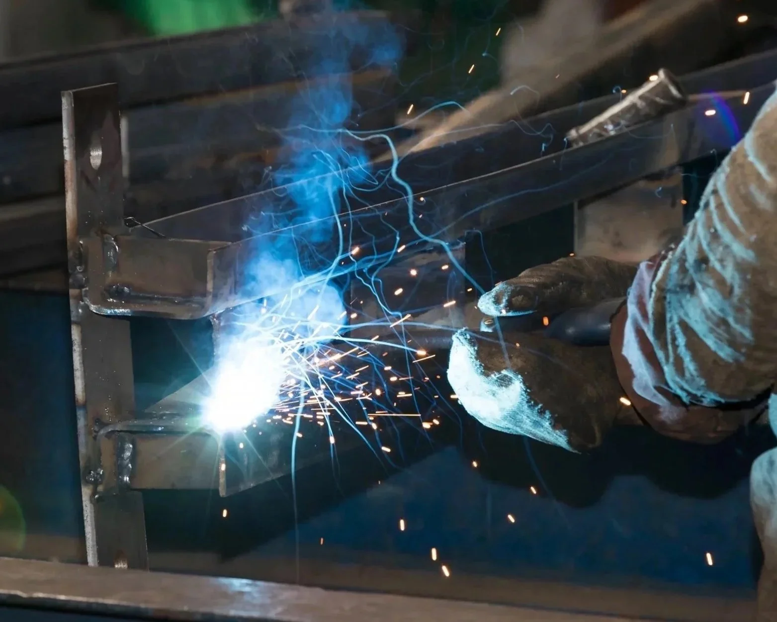 A person welding metal, creating sparks and blue arcs of electricity.