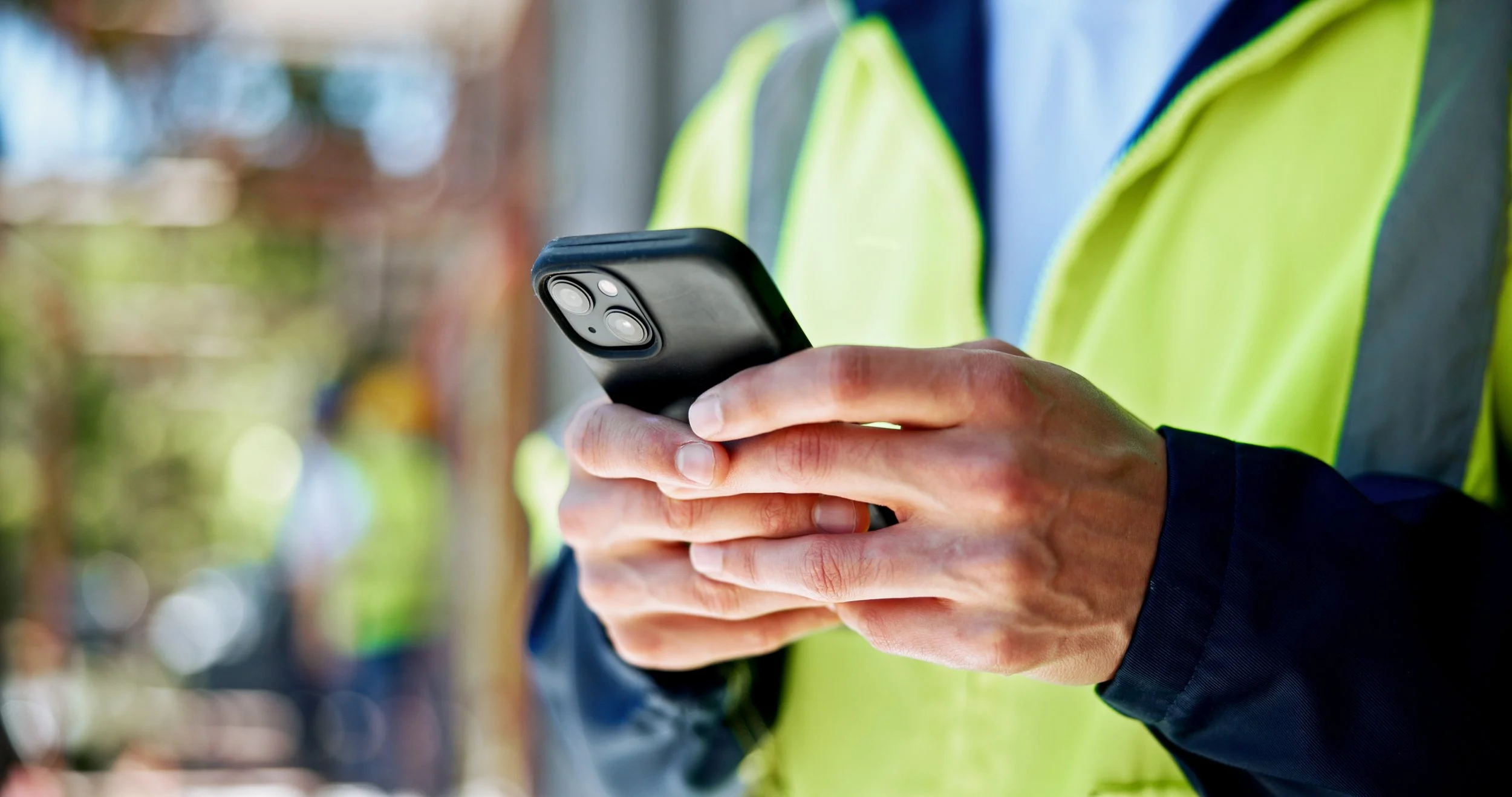 A person wearing a yellow safety vest and navy jacket holding a smartphone.