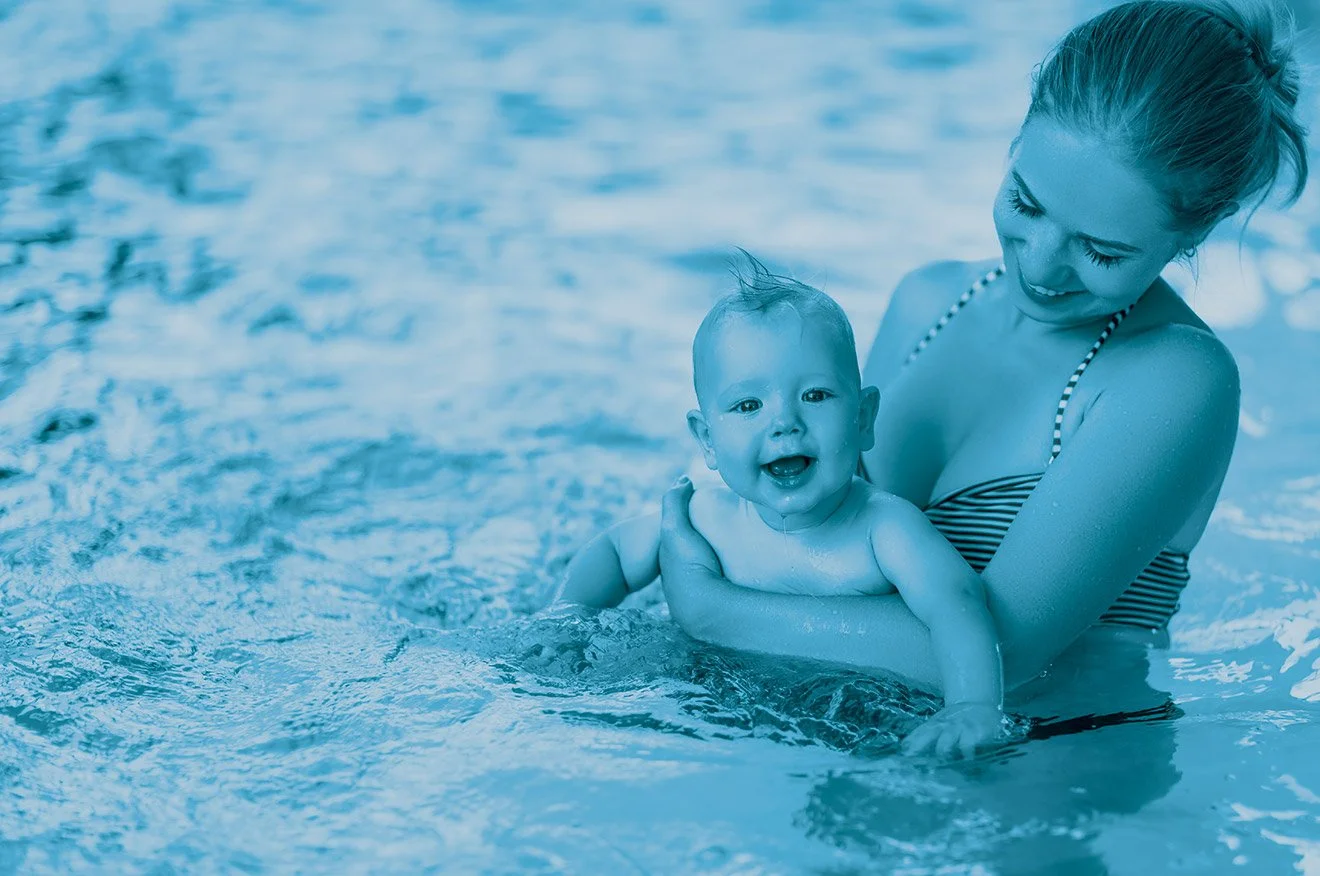 A smiling woman in a striped swimsuit holding a happy baby in swimming pool water.