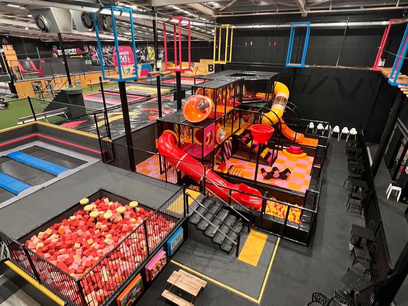 Indoor trampoline park with various colorful play structures, slides, foam pits, and trampolines