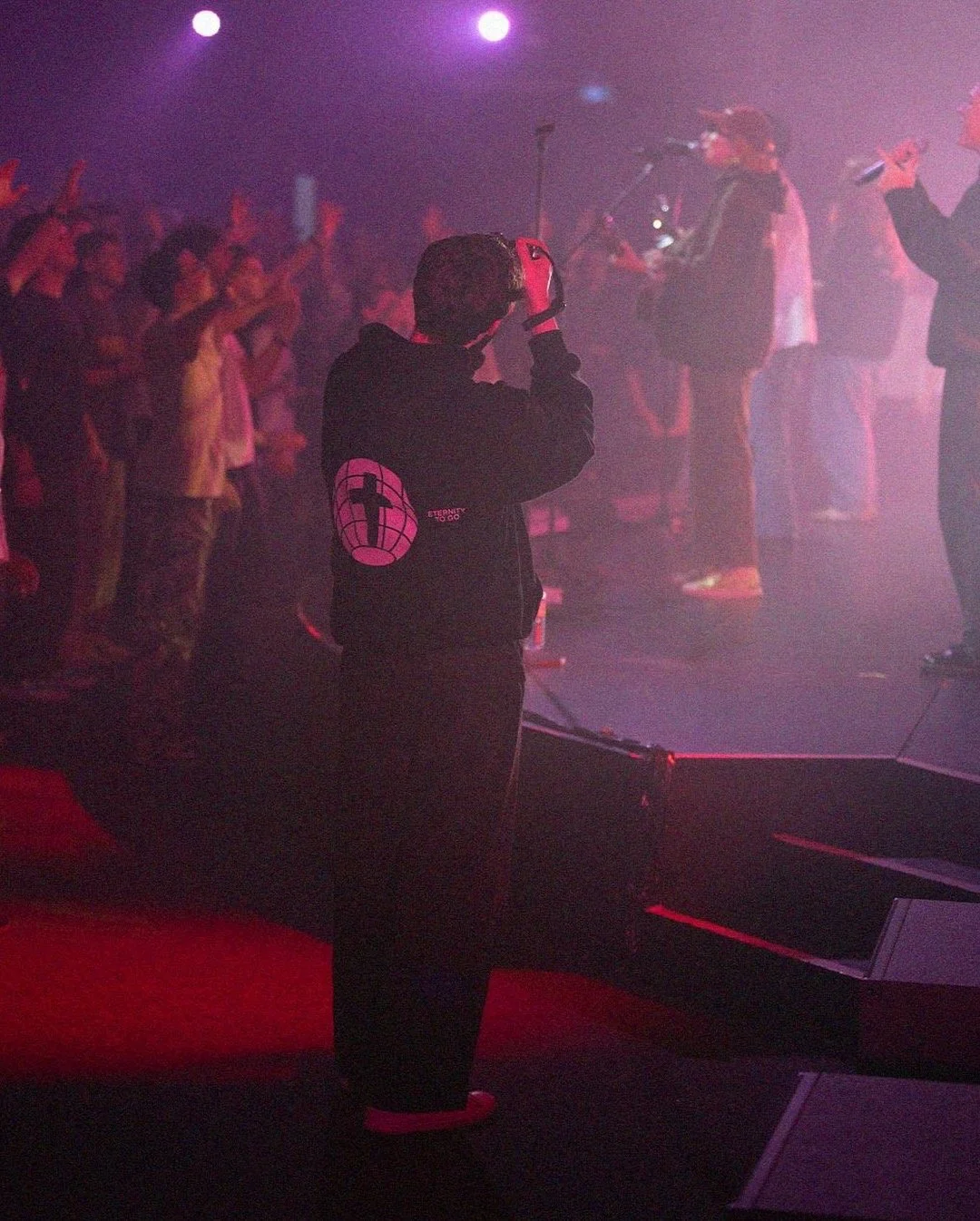 Founder of Joystudios captures a performer onstage under red and purple lights as the crowd watches.