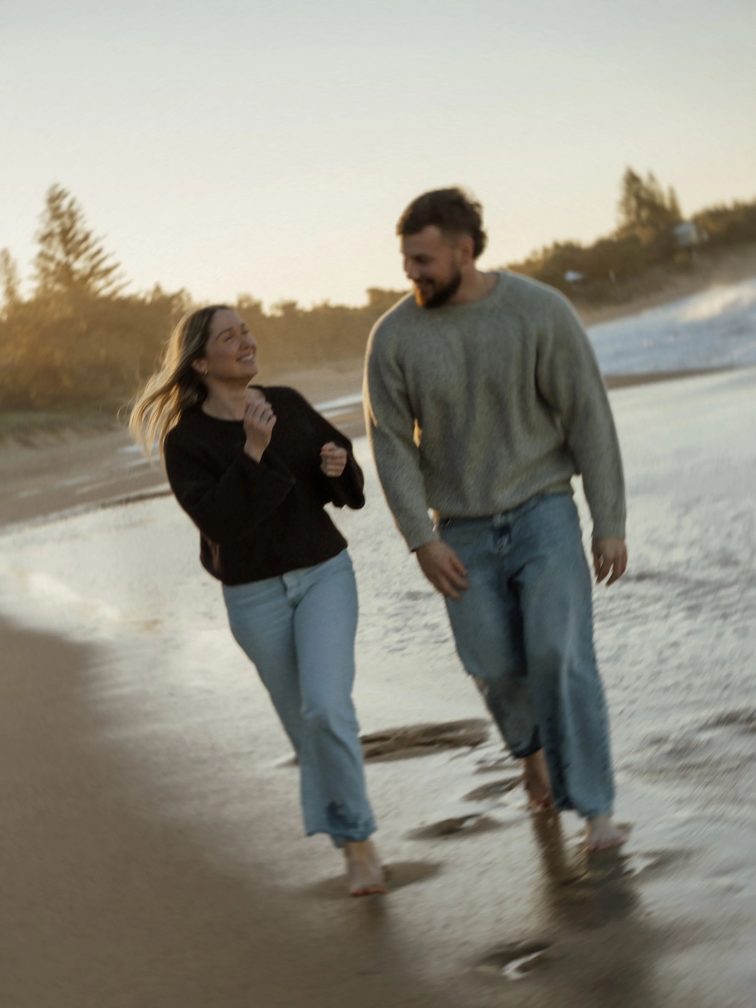 Smiling couple walking together along a beach at sunset.