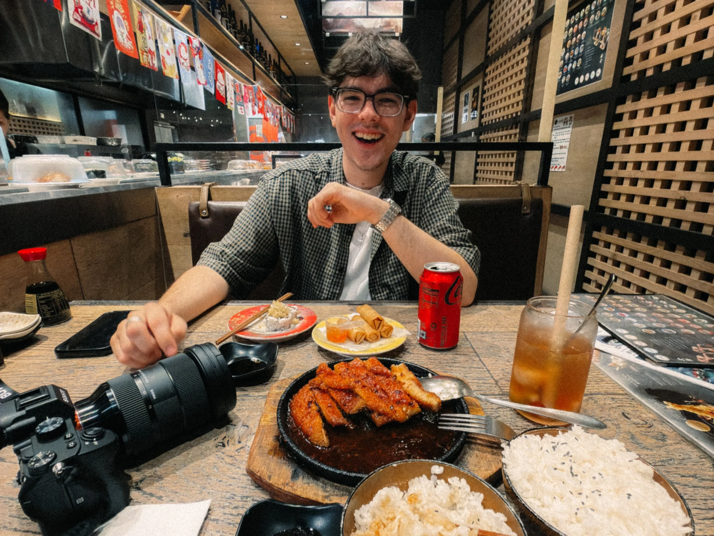 Founder of Joystudios dining at a Japanese restaurant with sushi, fried food, rice, drinks, and a camera on the table