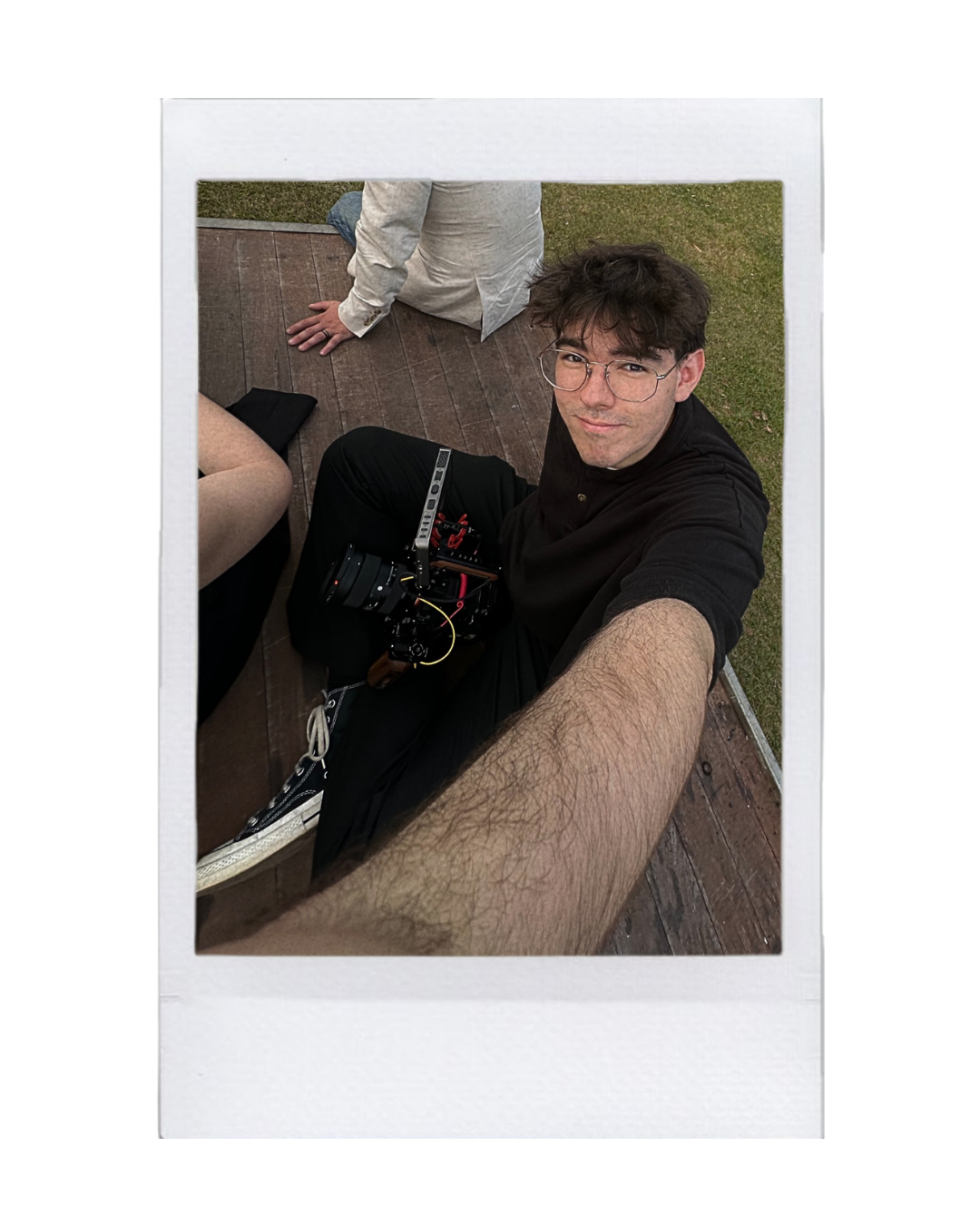 Founder of Joystudios, wearing glasses, takes a selfie while sitting on a wooden deck with a camera rig, joined by two partially visible people.