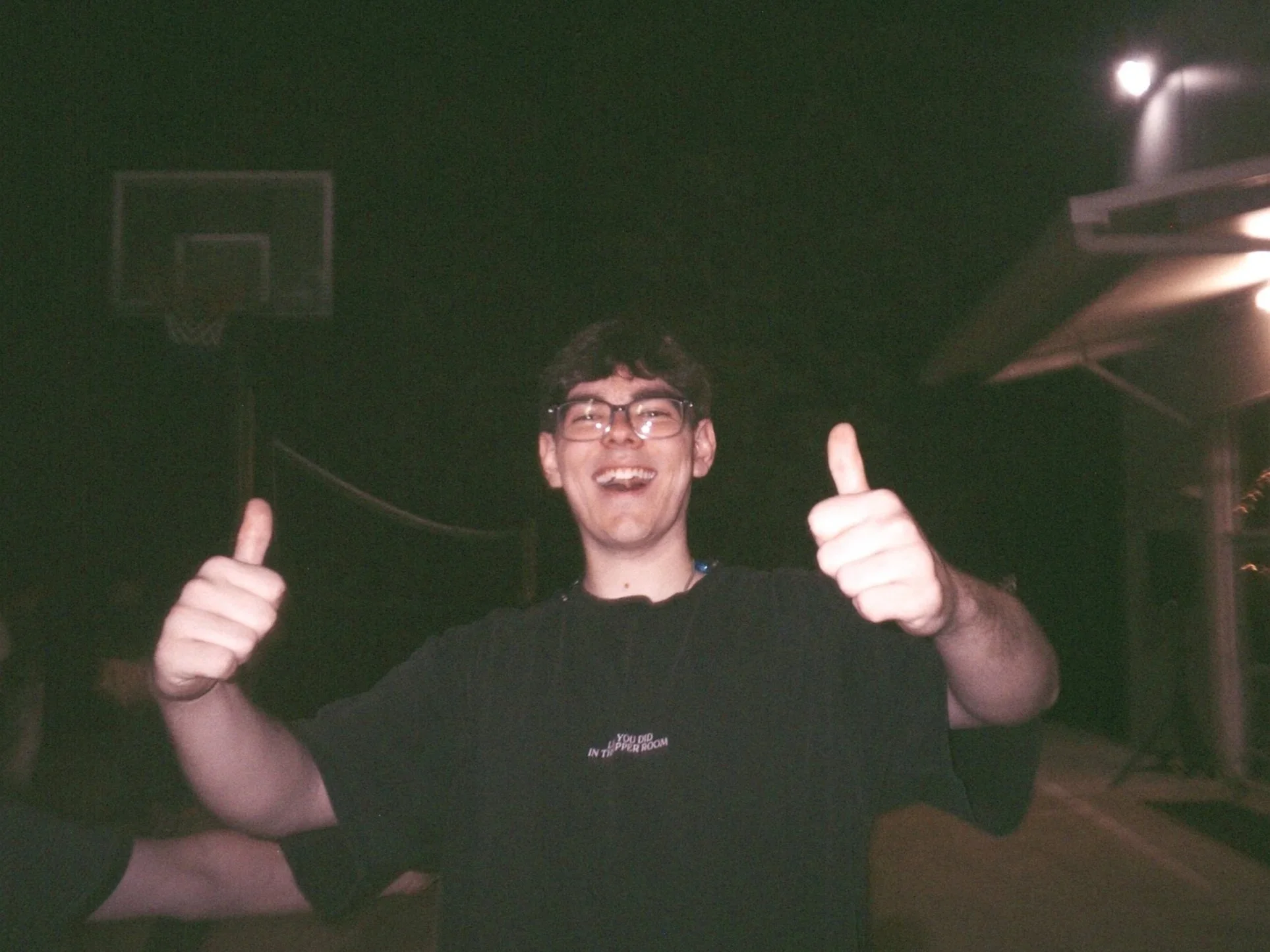 Founder of Joystudios, smiling wearing glasses, gives two thumbs up outdoors at night.