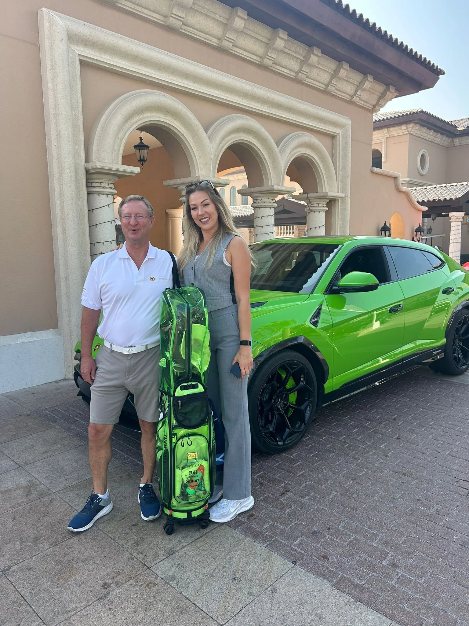 Two people standing next to a bright green sports car and a tennis bag in front of a beige building with arches.