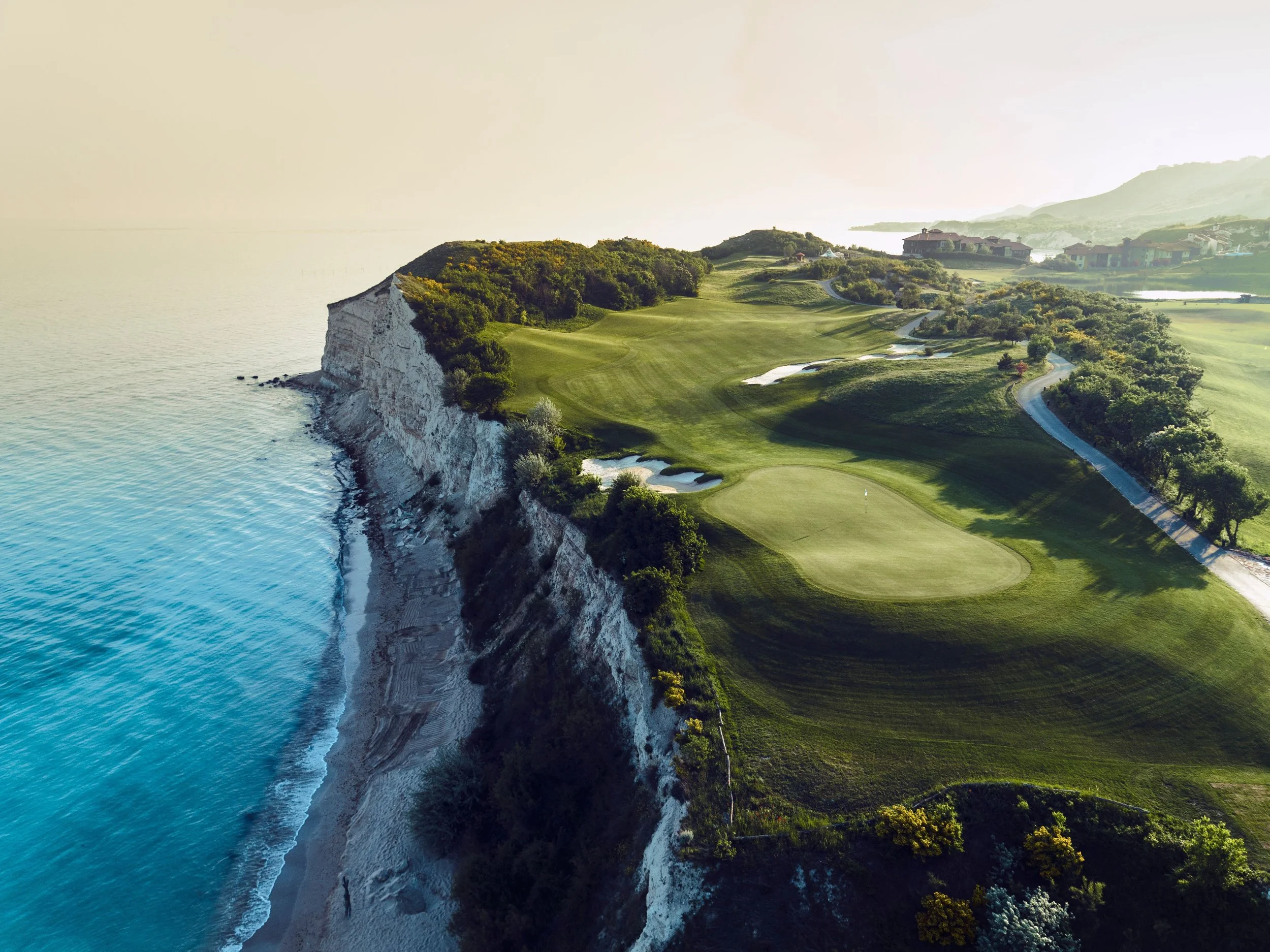 A scenic golf course on white chalk cliffs overlooking the ocean at sunset