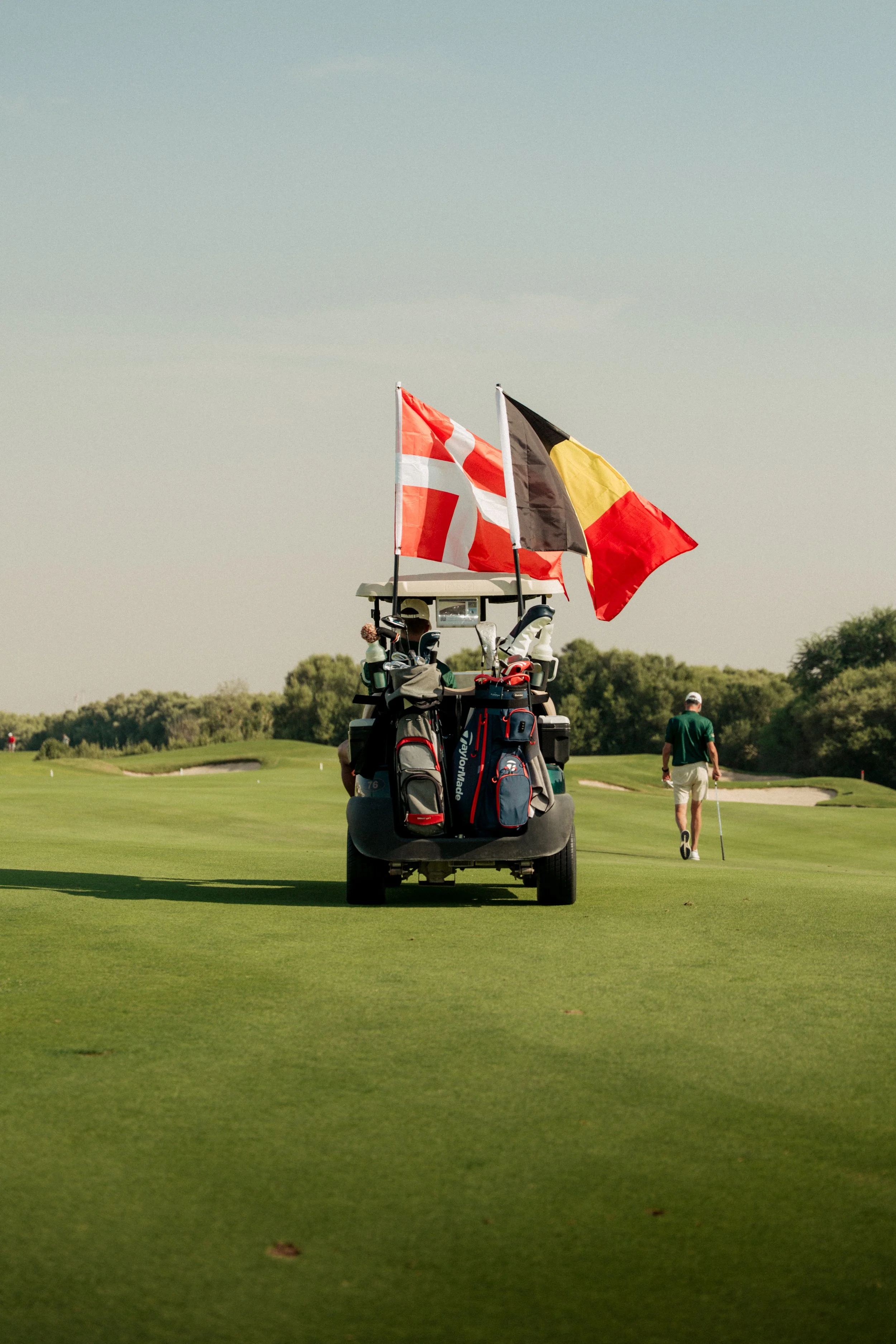 Golf course with golf bags, flags, and a person walking with a golf club in the background.