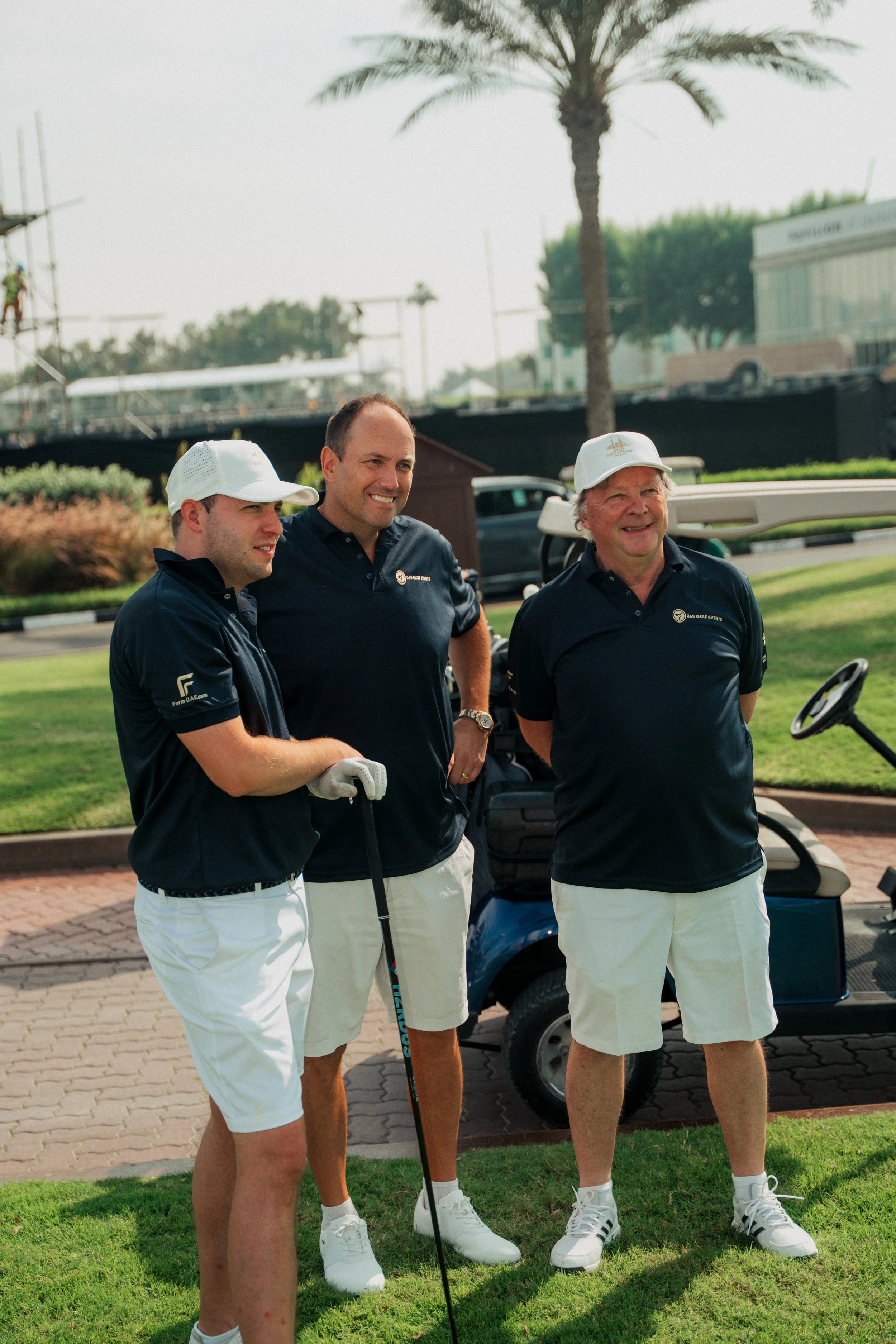 Three men standing on a golf course, posing for a photo, with a golf cart and palm trees in the background.