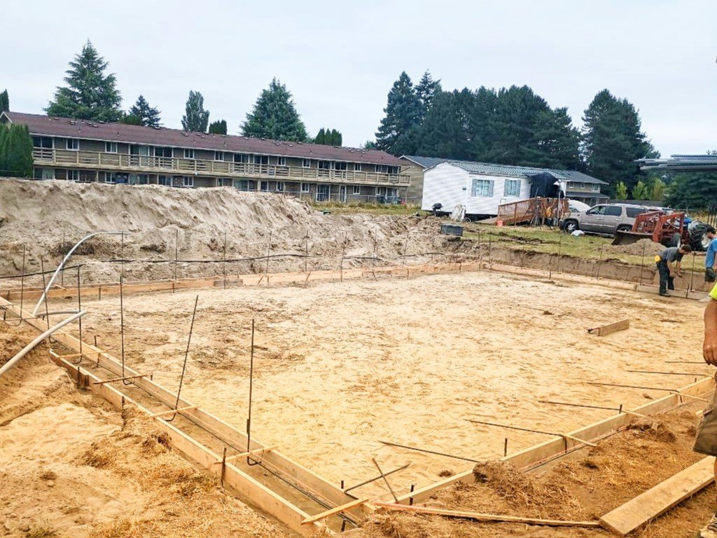 Formwork begins over flattened earth with wooden boards and rebar laid out before foundation pour. 