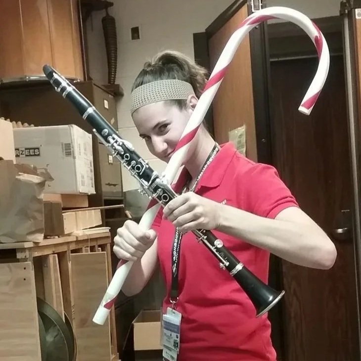 Photo of a woman wielding a clarinet and a candy cane in an X shape in front of her body