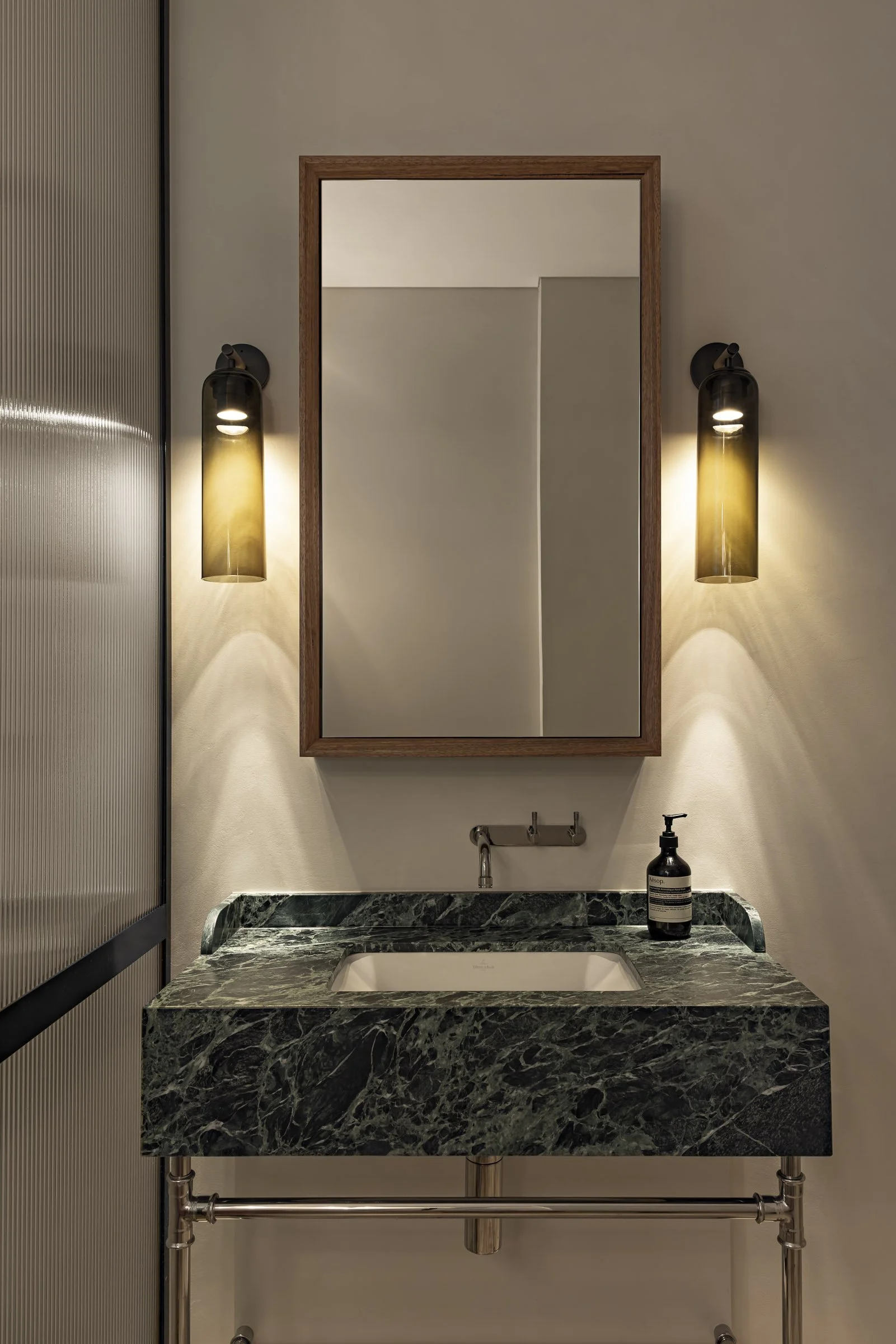 A bathroom vanity with a green marble countertop, mirror, and two wall-mounted black and gold light fixtures.