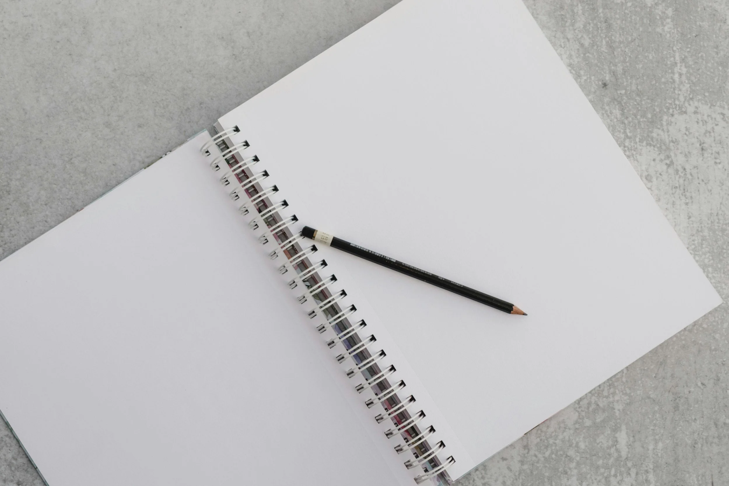 Open blank spiral notebooks with a black pencil resting on top, placed on a light grey textured surface.