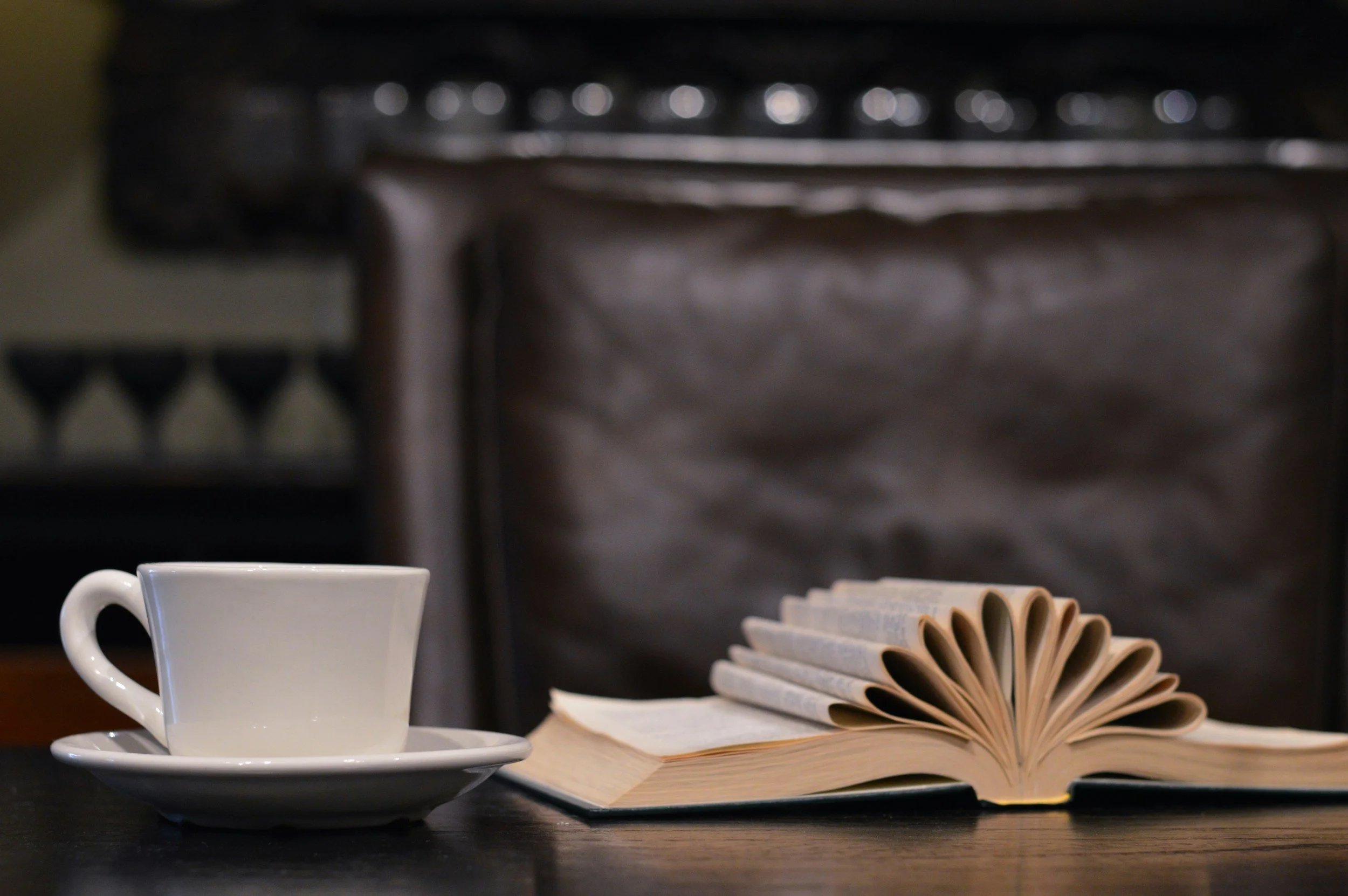 A white coffee cup with a saucer next to an open book with pages curled.