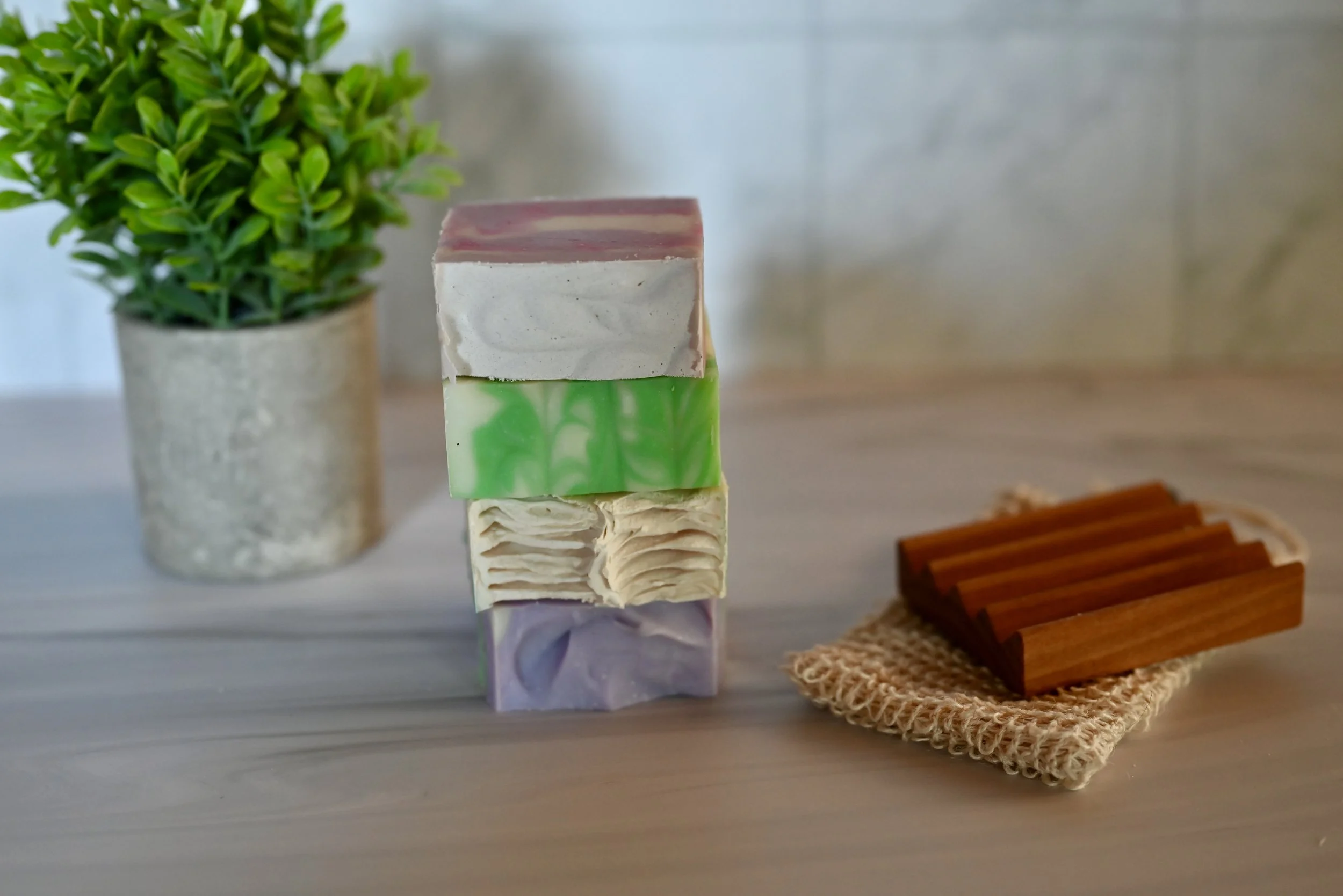 A stack of 4 of our handmade goat milk soaps stand next to a soap deck and soap saver.