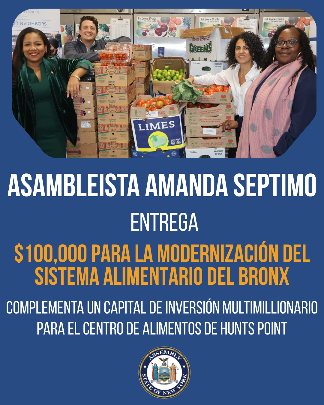 Group of four women and one man standing behind a table of boxes filled with tomatoes, limes, and other vegetables inside a community center or food bank. They are smiling, and some are holding papers, with posters about fruits and food safety in the
