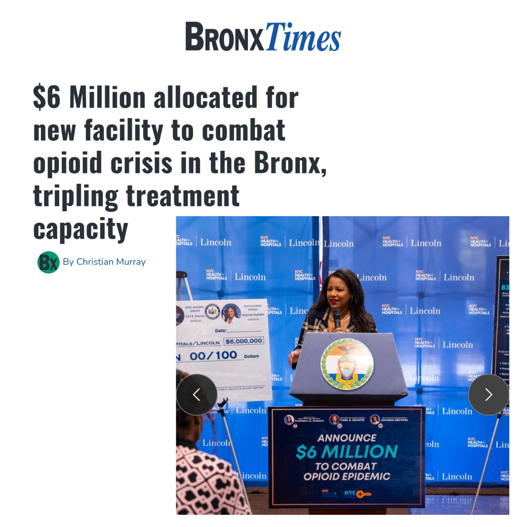 A woman speaking at a press conference with a large check for $6 million in front of a blue backdrop with NYC Health + Hospitals and Lincoln logos. The check is displayed as part of an announcement to combat the opioid crisis in the Bronx.