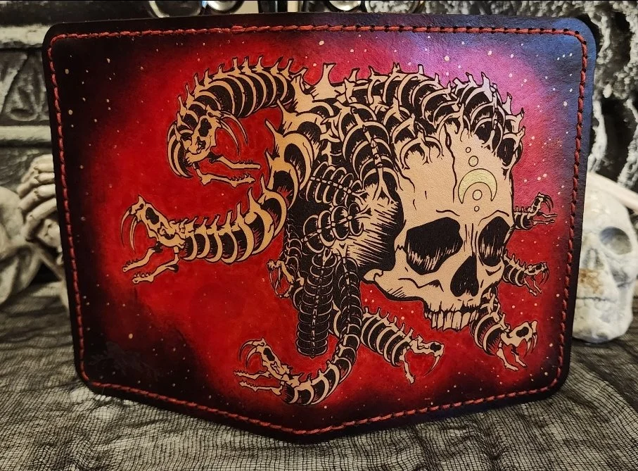 A wallet with a vivid red and purple background, featuring a black and beige tattoo-style design of a skull with multiple snakes merging from it.