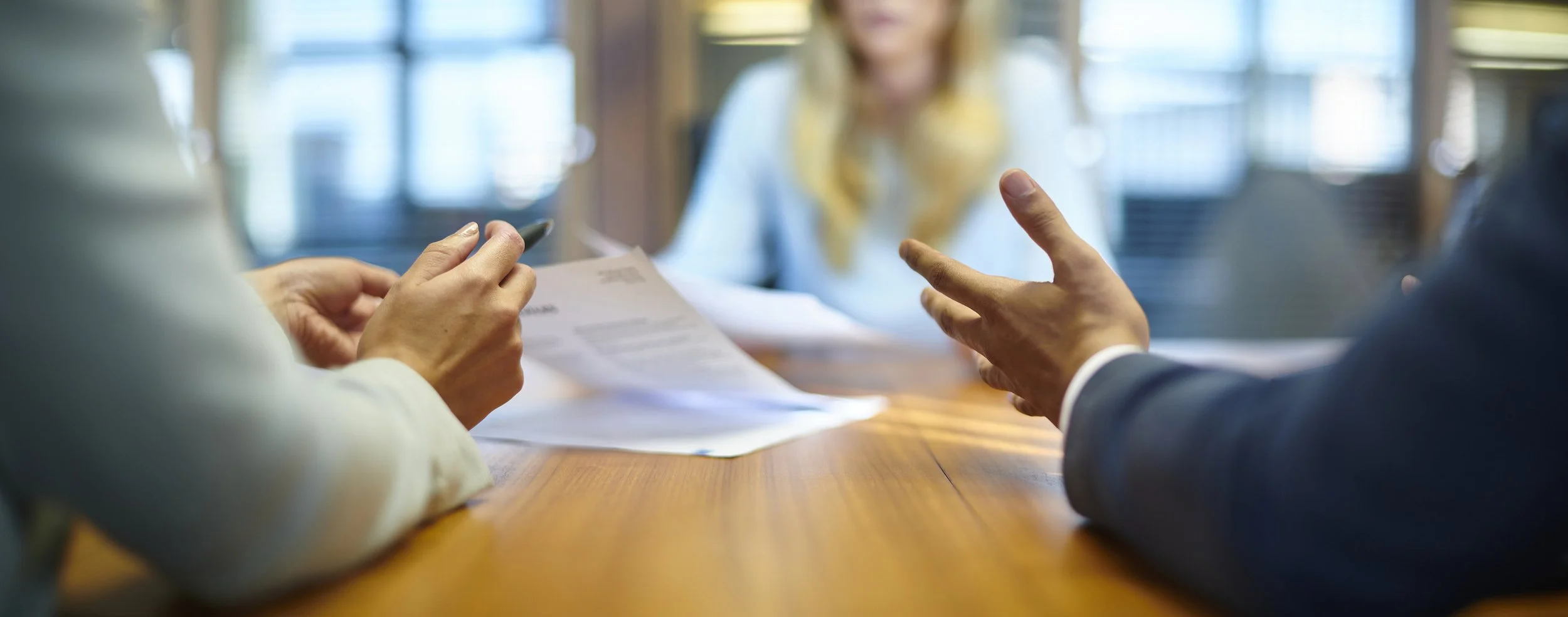 Business professionals in a discussion at a meeting, with papers on a wooden conference table.