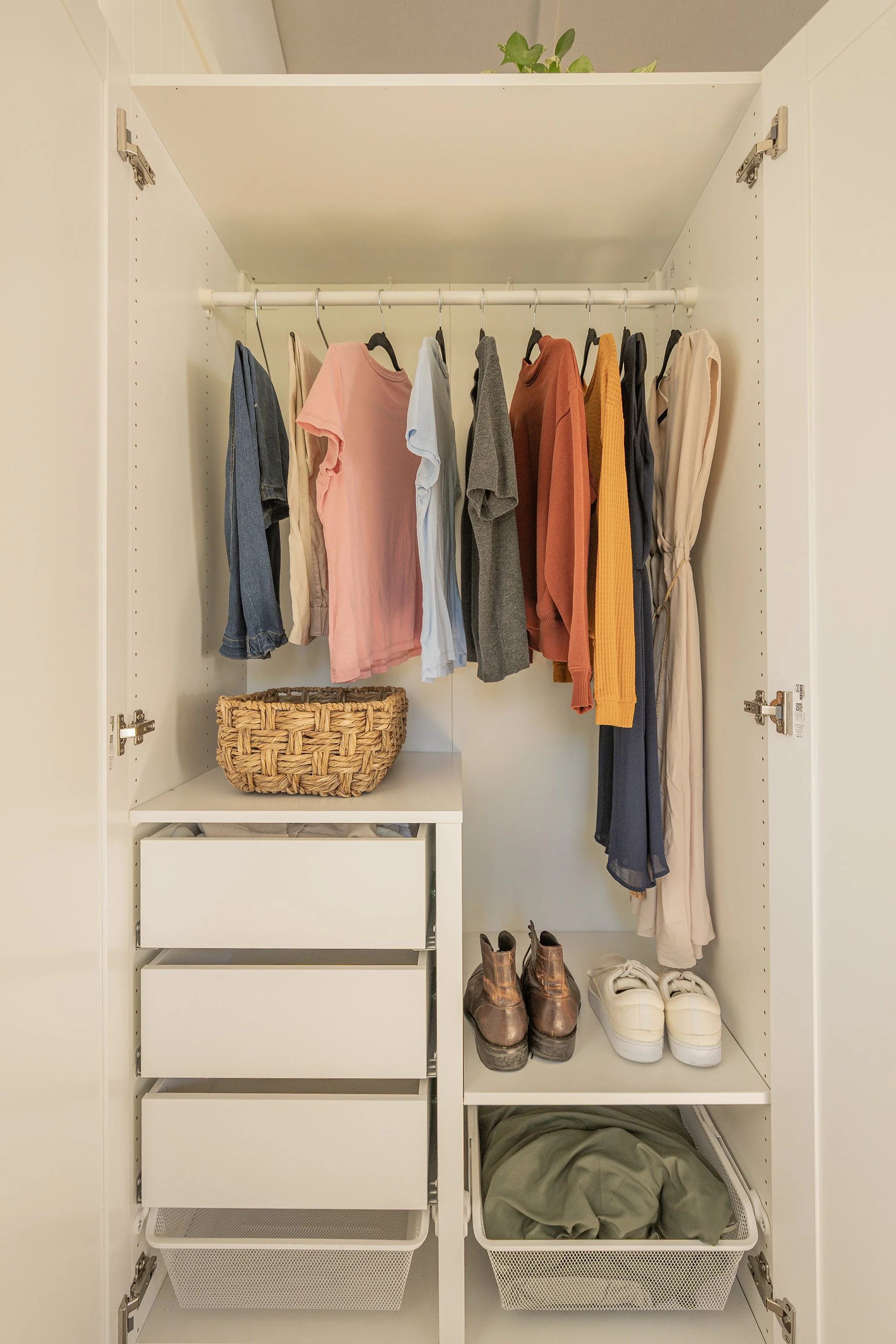 Open wardrobe with hanging clothes, a woven basket, shoes, and storage bins