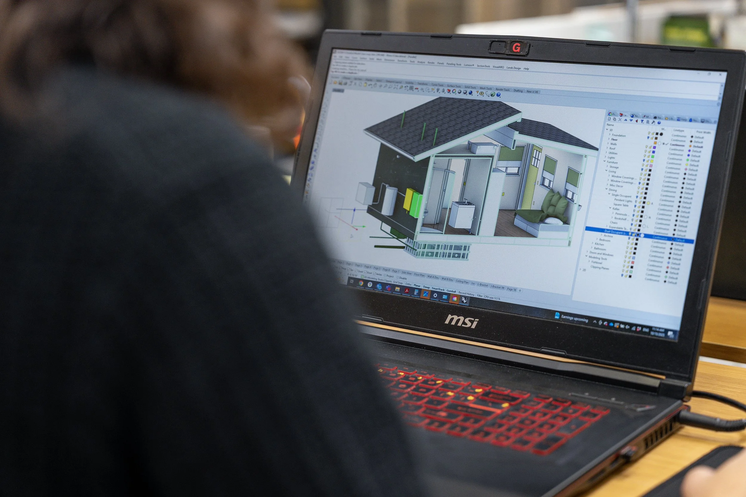 A person working on a laptop displaying a 3D house design in CAD software.