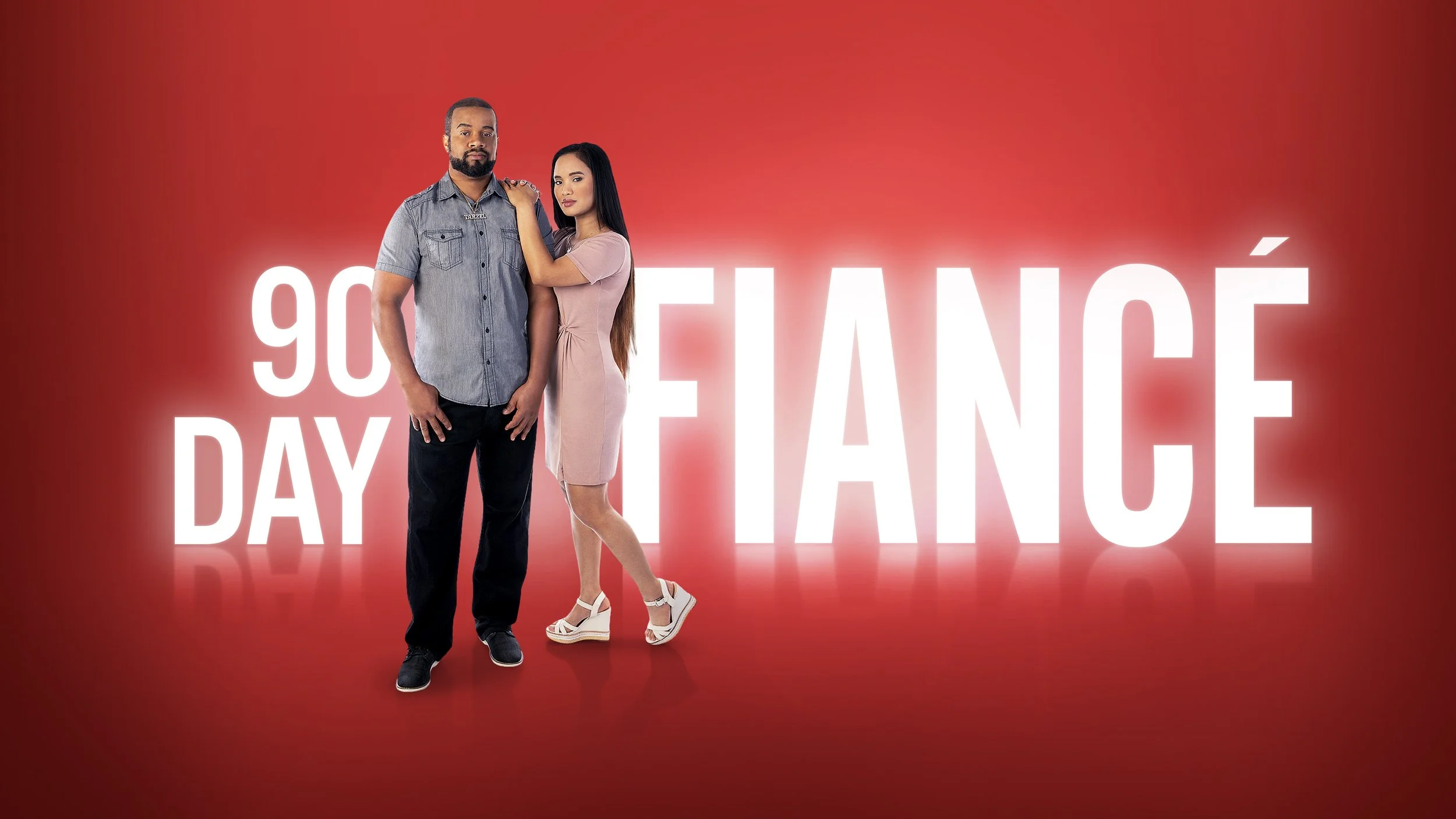 A man and woman standing together in front of a red background with white text that reads '90 DAY FIANCÉ