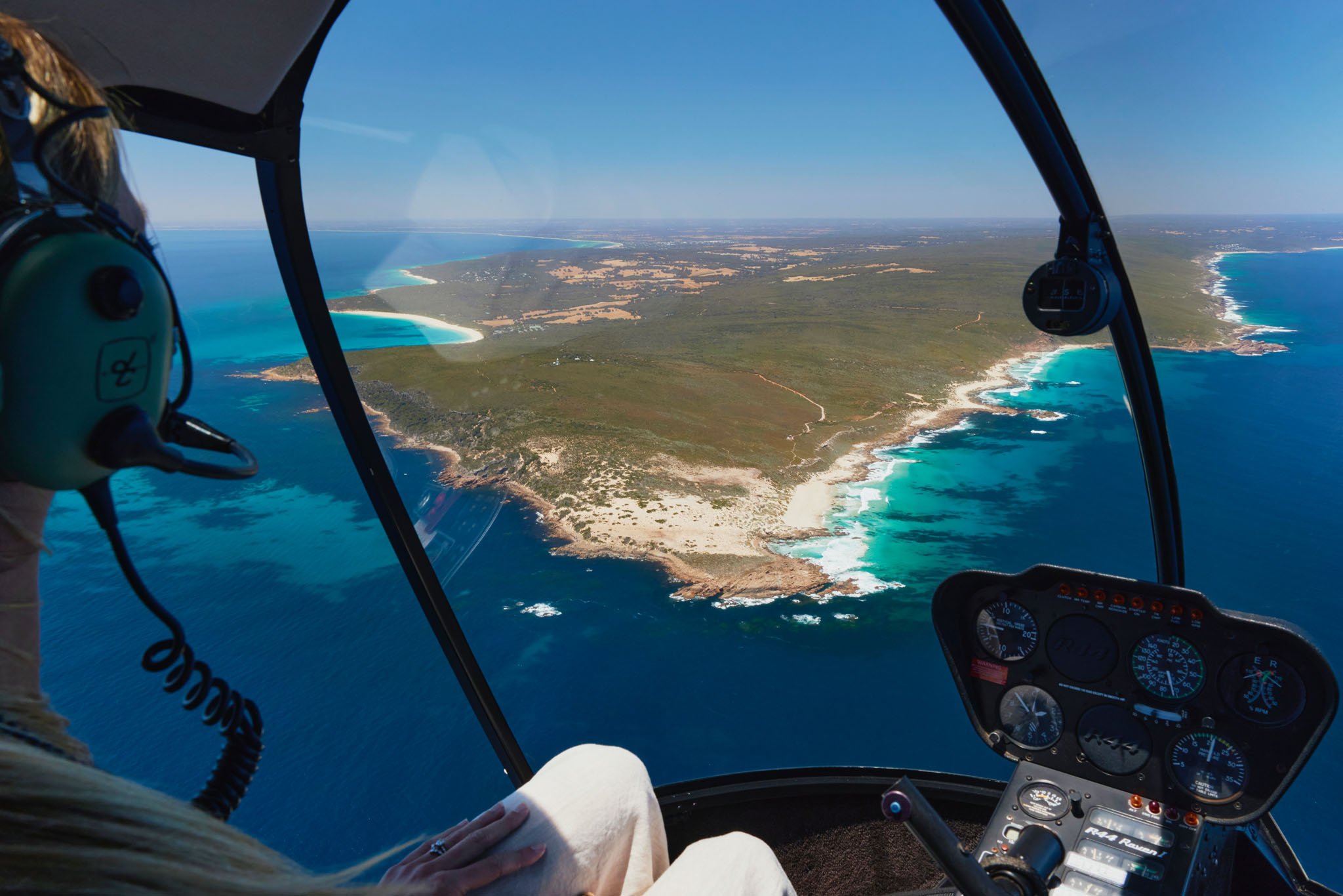 Inside a helicopter cockpit showing flight instruments and a view of coastline and ocean below.