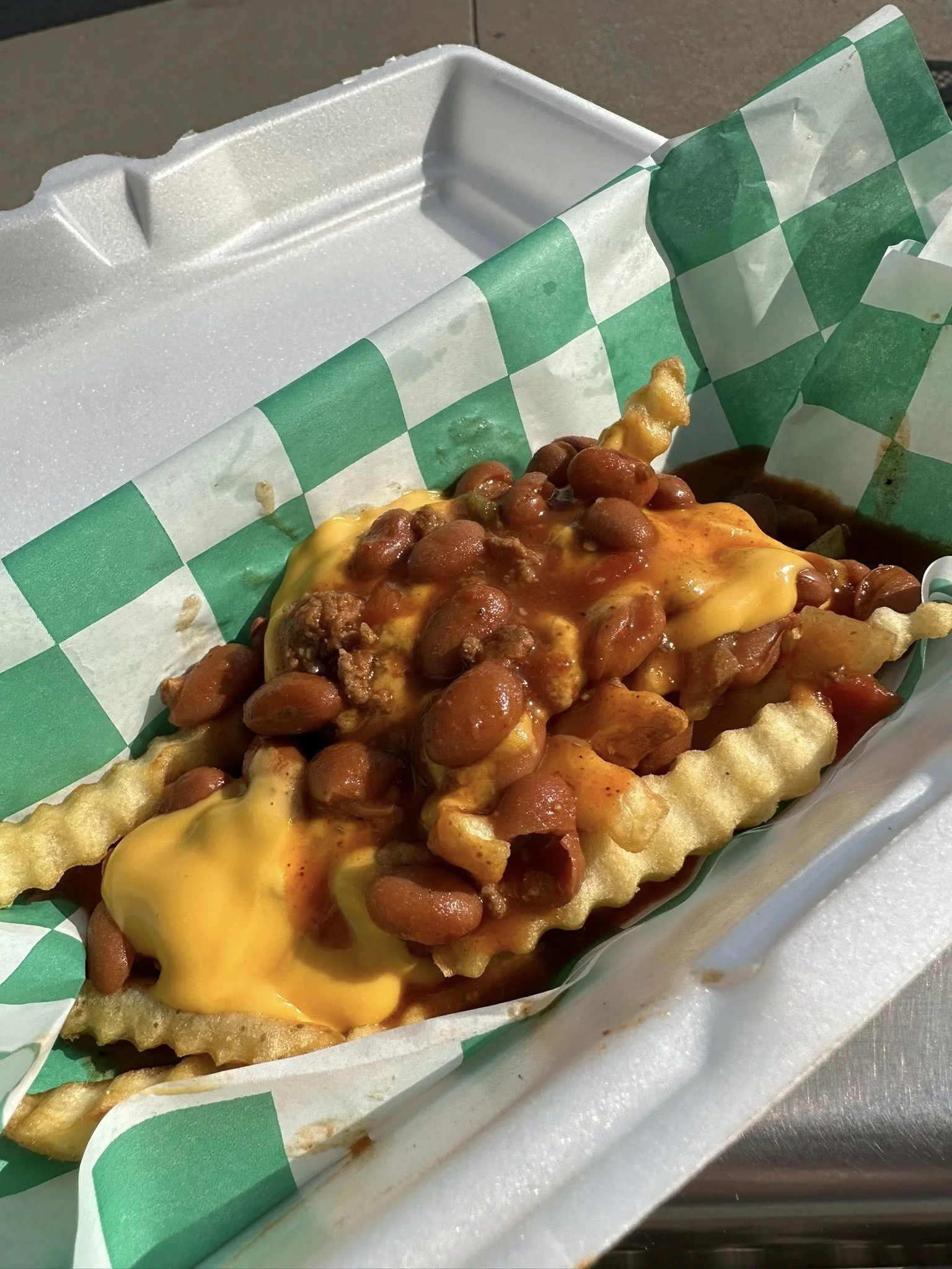 Fried waffle topped with baked beans and melted cheese in takeout container.