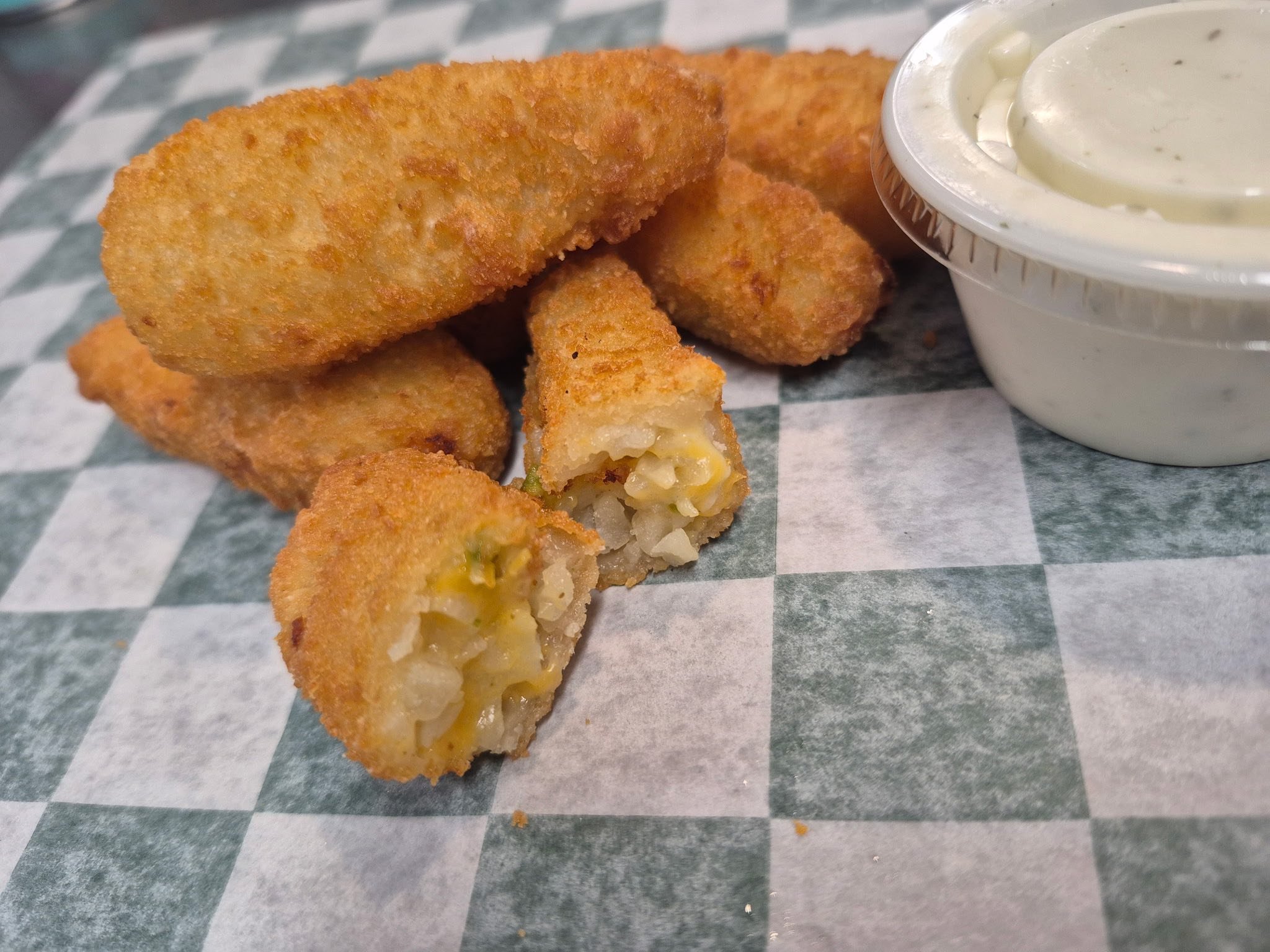 Fried jalapeno poppers with a side of ranch dressing on a checkered paper lining.