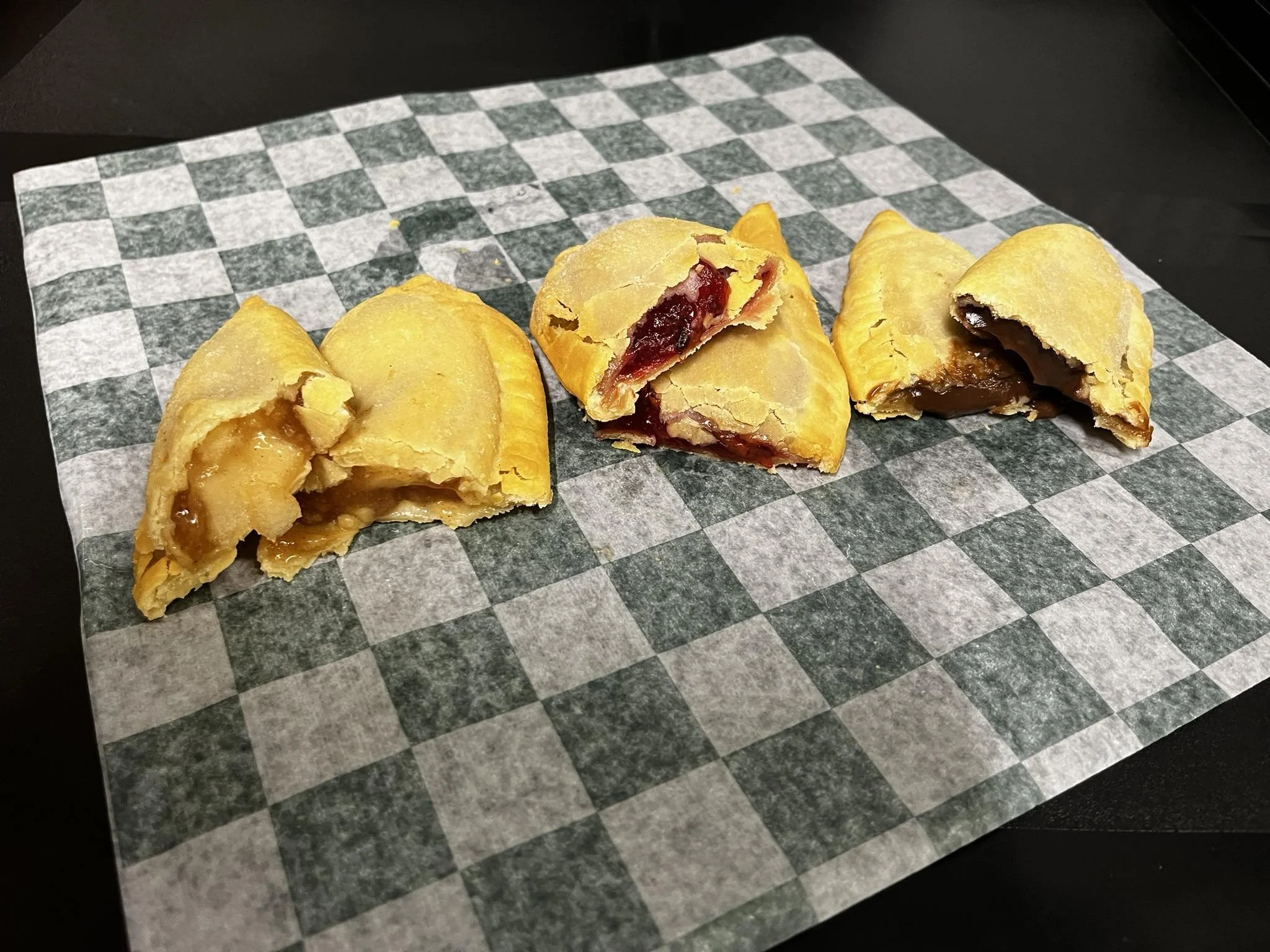 Three apple hand pies with different fillings on a checkered paper on a black surface.