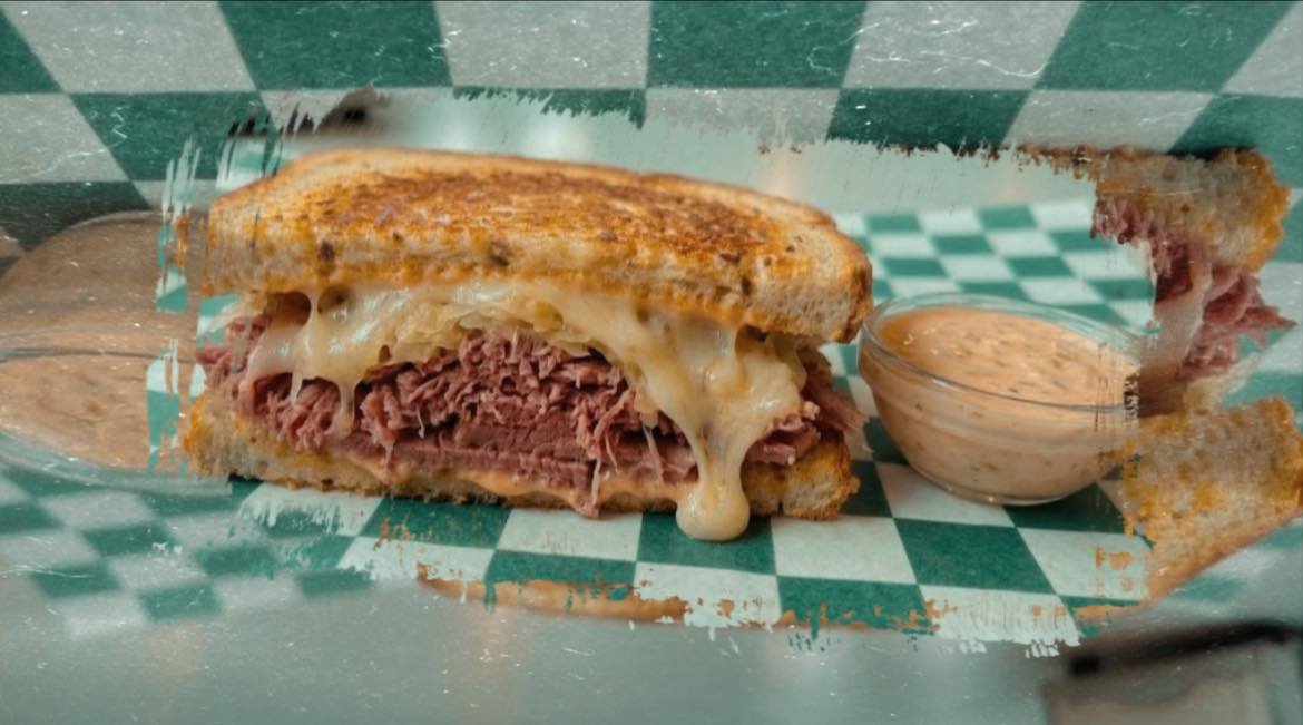 Grilled cheese sandwich with roast beef and cheese, served with a sauce on the side.