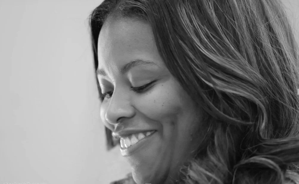 Close-up of a woman smiling with her eyes closed and head slightly turned to the side, in black and white.