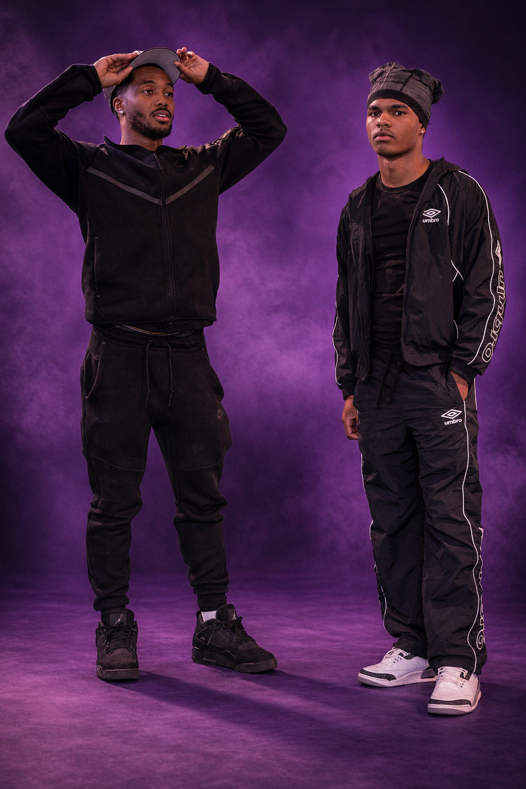 Two young men standing against a purple smoky background, one adjusting his baseball cap and the other with hands in pockets, both dressed in black athletic clothing.