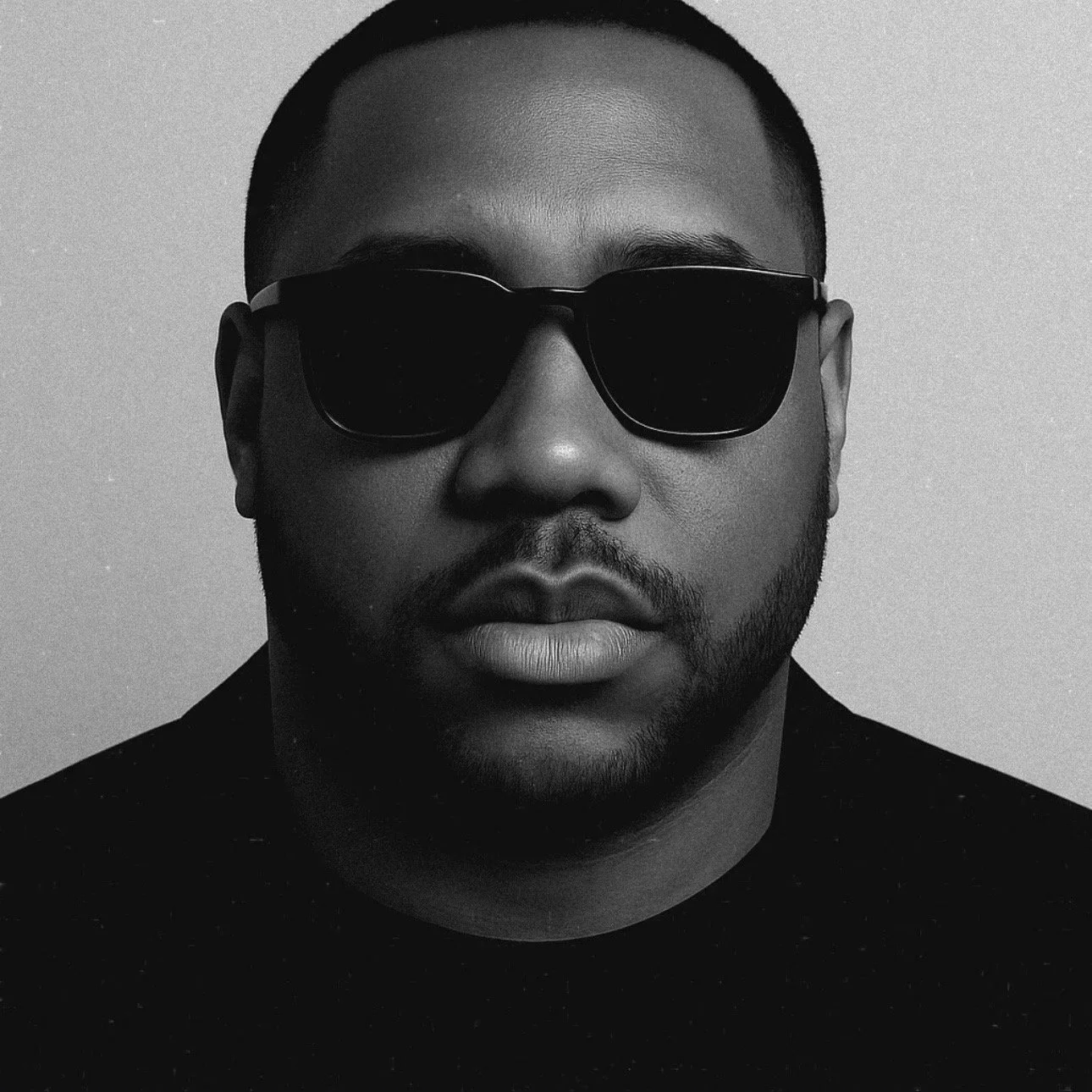 Portrait of a man wearing sunglasses and a black shirt, in black and white.