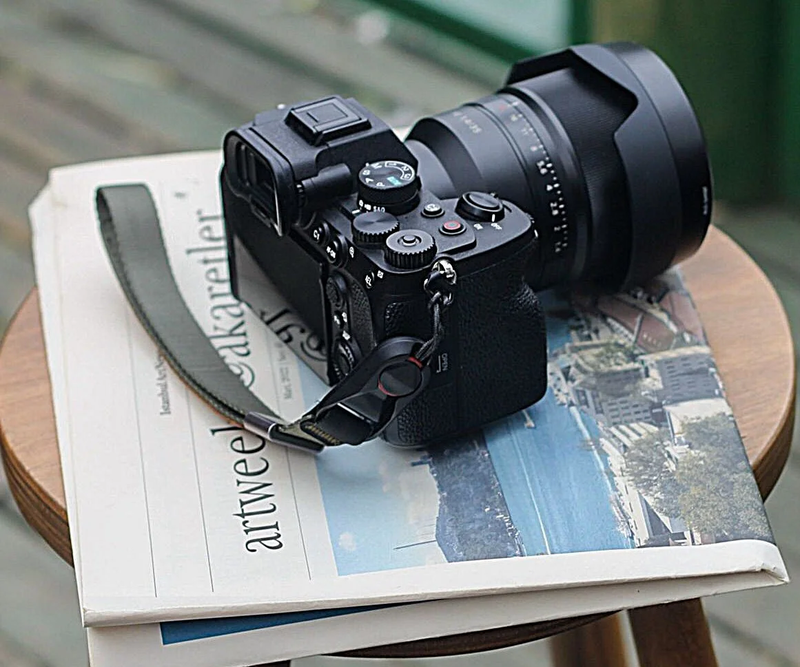 A camera with a large lens resting on a newspaper on a wooden side table.
