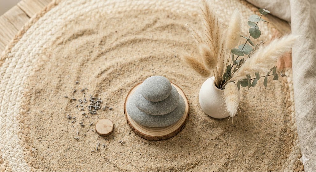 Ein Stapel von drei glatten Steinen, die am Strand im Sand balanciert sind, Trockenblumen im Hintergrund, Boho-Stil.