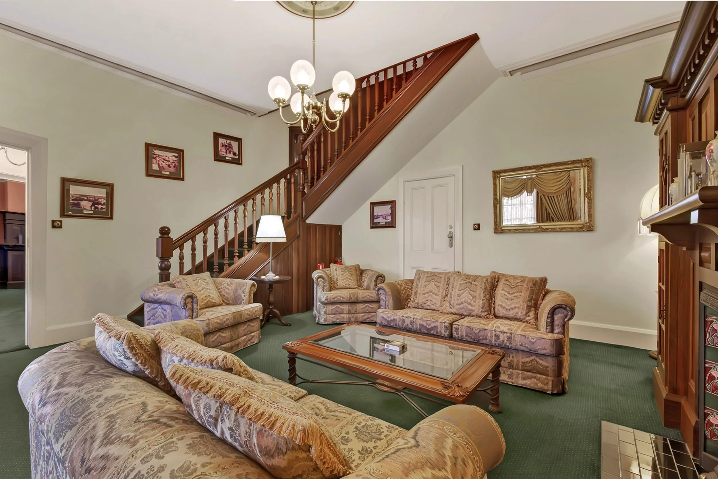 Traditional living room with vintage sofas, wooden staircase, chandelier, mirror, and fireplace.