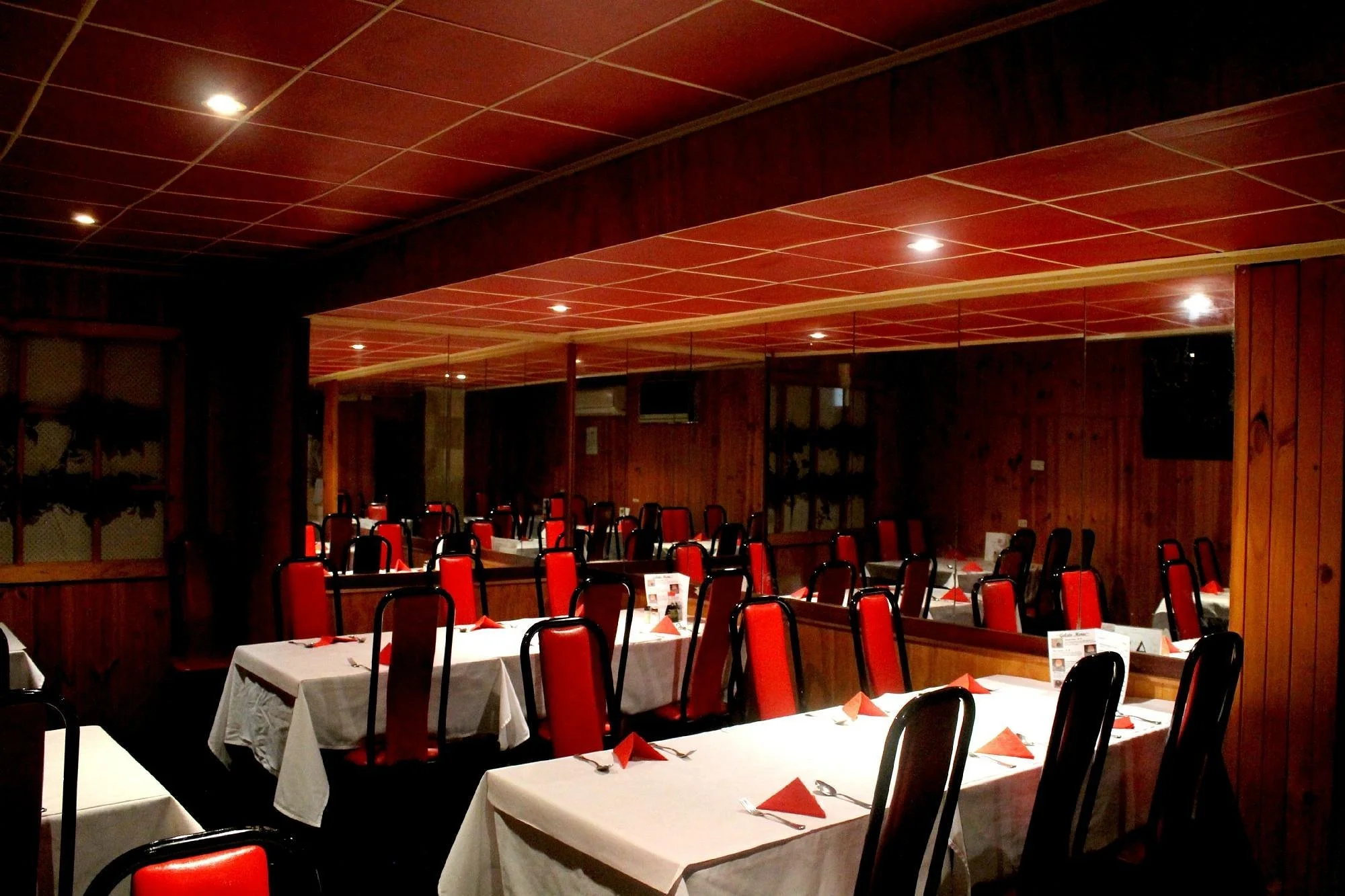 Empty restaurant dining area with red chairs, white tablecloths, and neatly folded red napkins at each place setting.