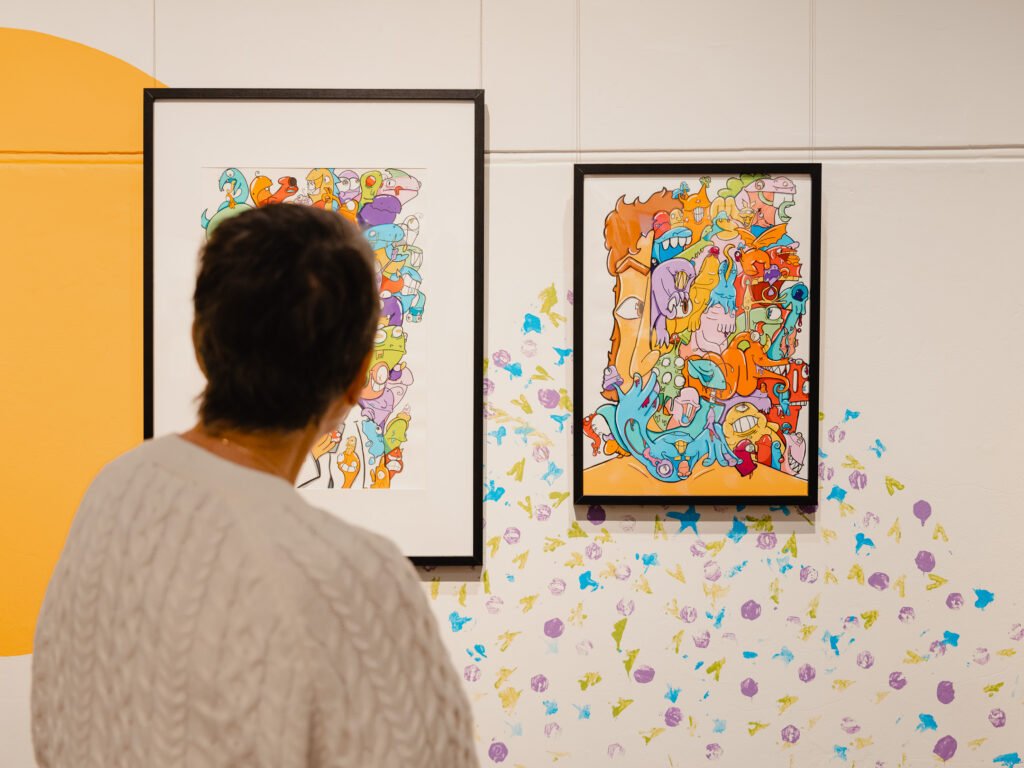 A person observing colorful abstract artwork in an art gallery with paint splatters on the wall.