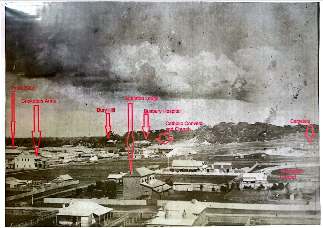 Historical black and white photograph of a town with marked locations including Rose Hotel, Cricketers Arms, Bury Hill, Gritten Lodge, Bunbury Hospital, Catholic Convent and Church, Cemetery, and Ground, with a dramatic stormy sky.