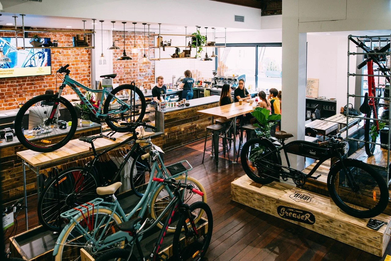Interior of a bicycle shop restaurant with bikes on display and customers dining at high tables.