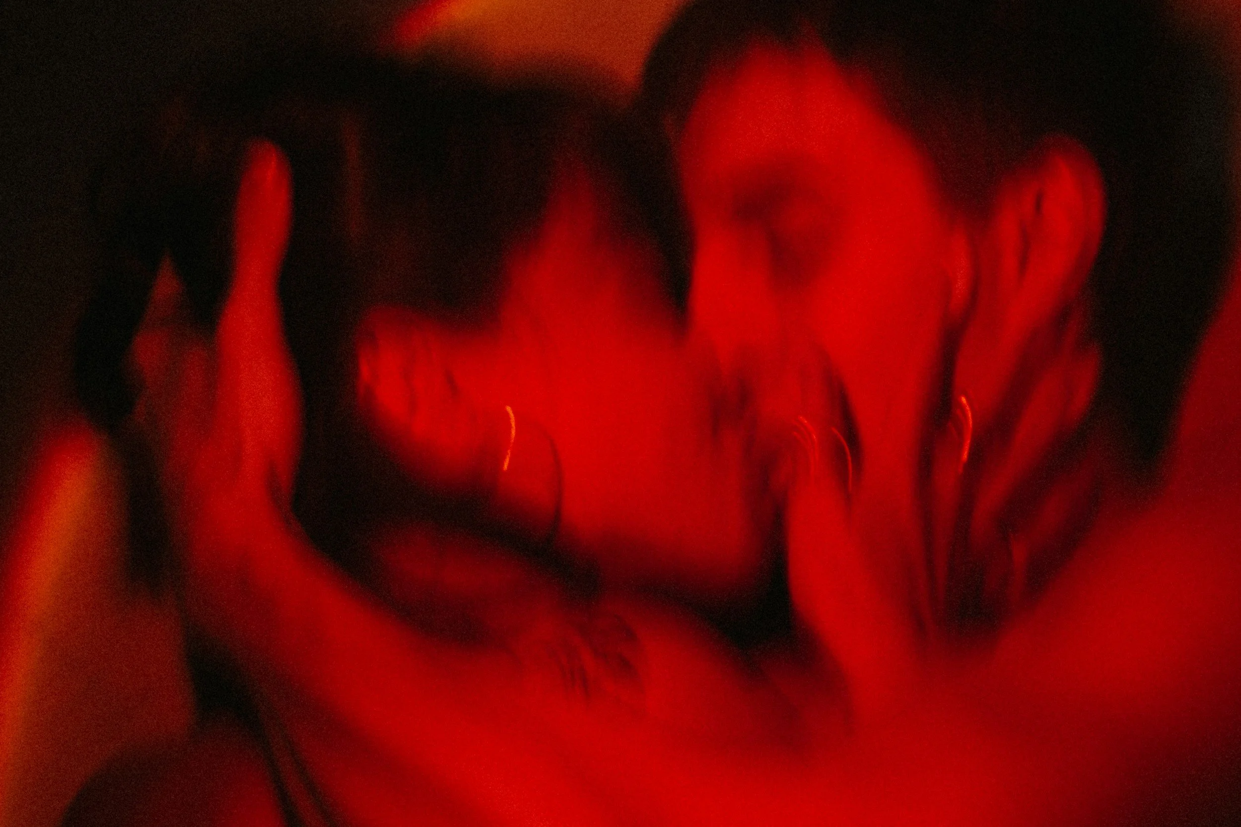 A close-up of a couple kissing with red lighting and blurred focus.