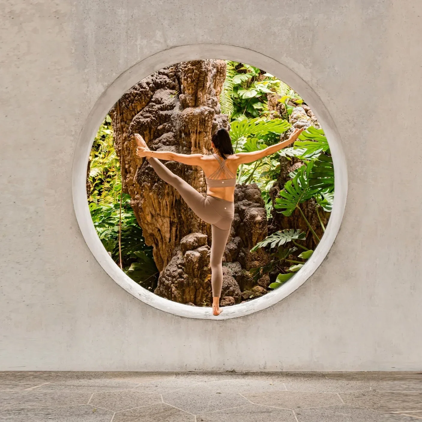 A person standing on a circular glassless window with her back facing the camera doing yoga pose
