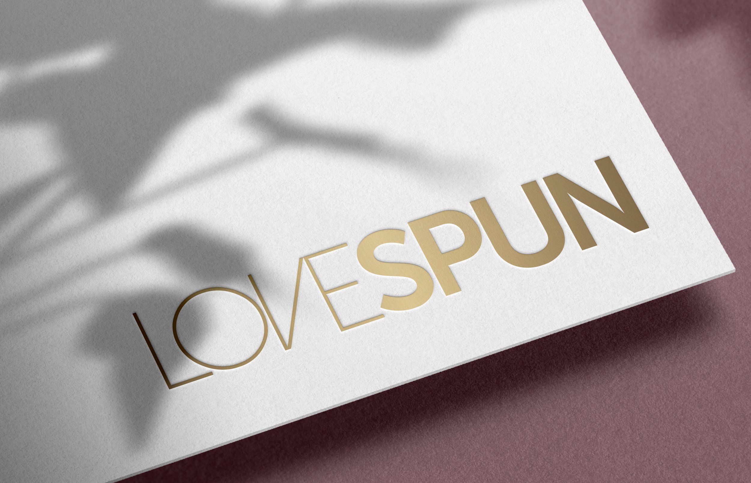 Lovespun luxurious gold color logo in white paper on a purple background and plant shadow casting over