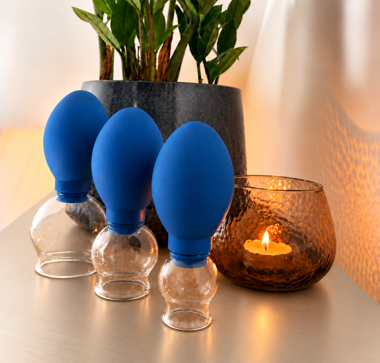 Drie blauwe glazen cuppingcups met een amberkleurige kaars op een zachte champagnekleurige tafel